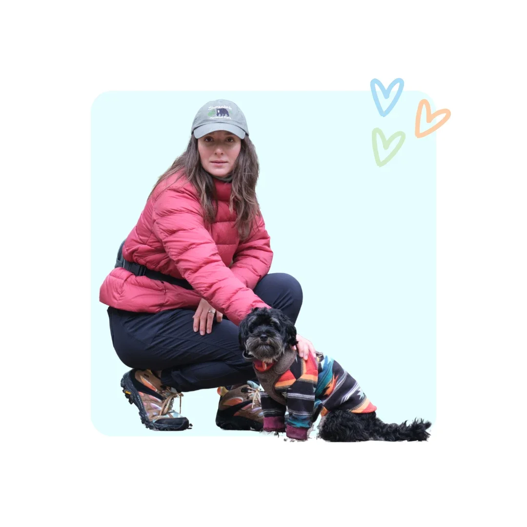 Dog sitter Taya on the UES wearing a pink puffer jacket and baseball cap, kneeling with a tiny black dog in a sweater