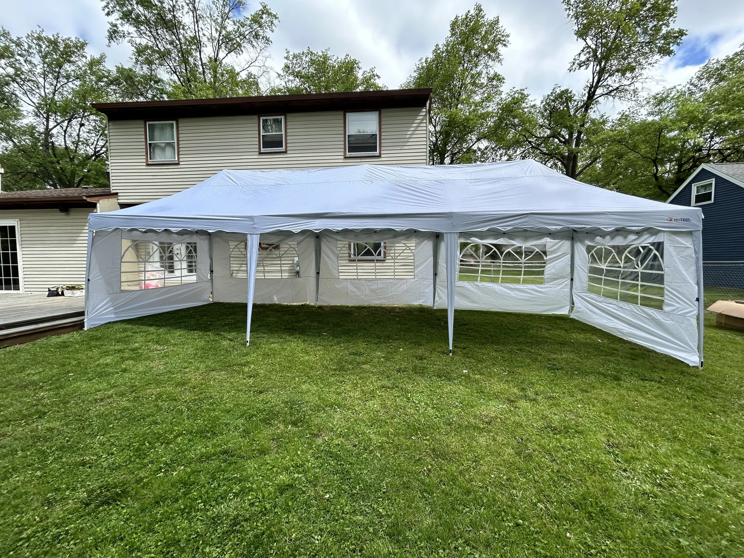 White outdoor event tent set up on a grassy backyard with houses and trees in the background.