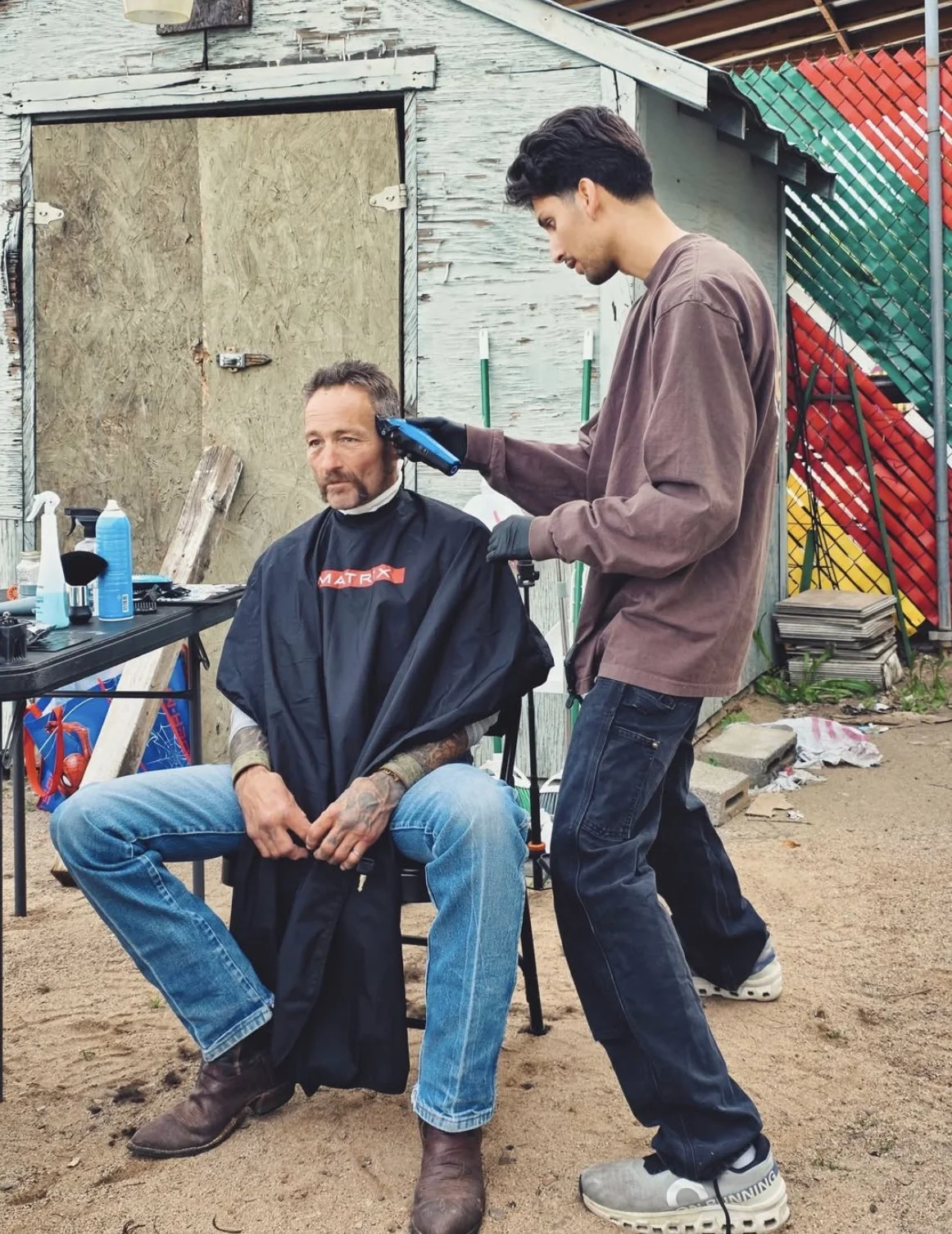 A man getting a haircut outdoors by a young barber.