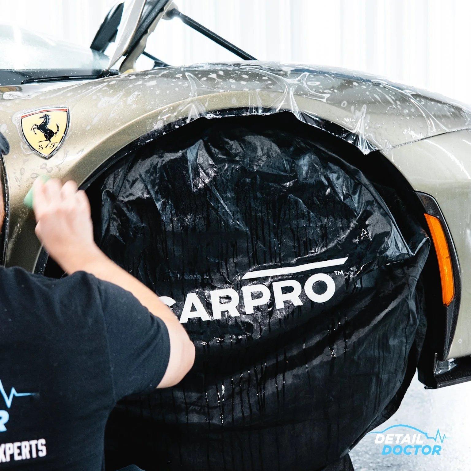 Person wrapping a luxury car with car protection film, with a Ferrari logo visible on the front of the car.