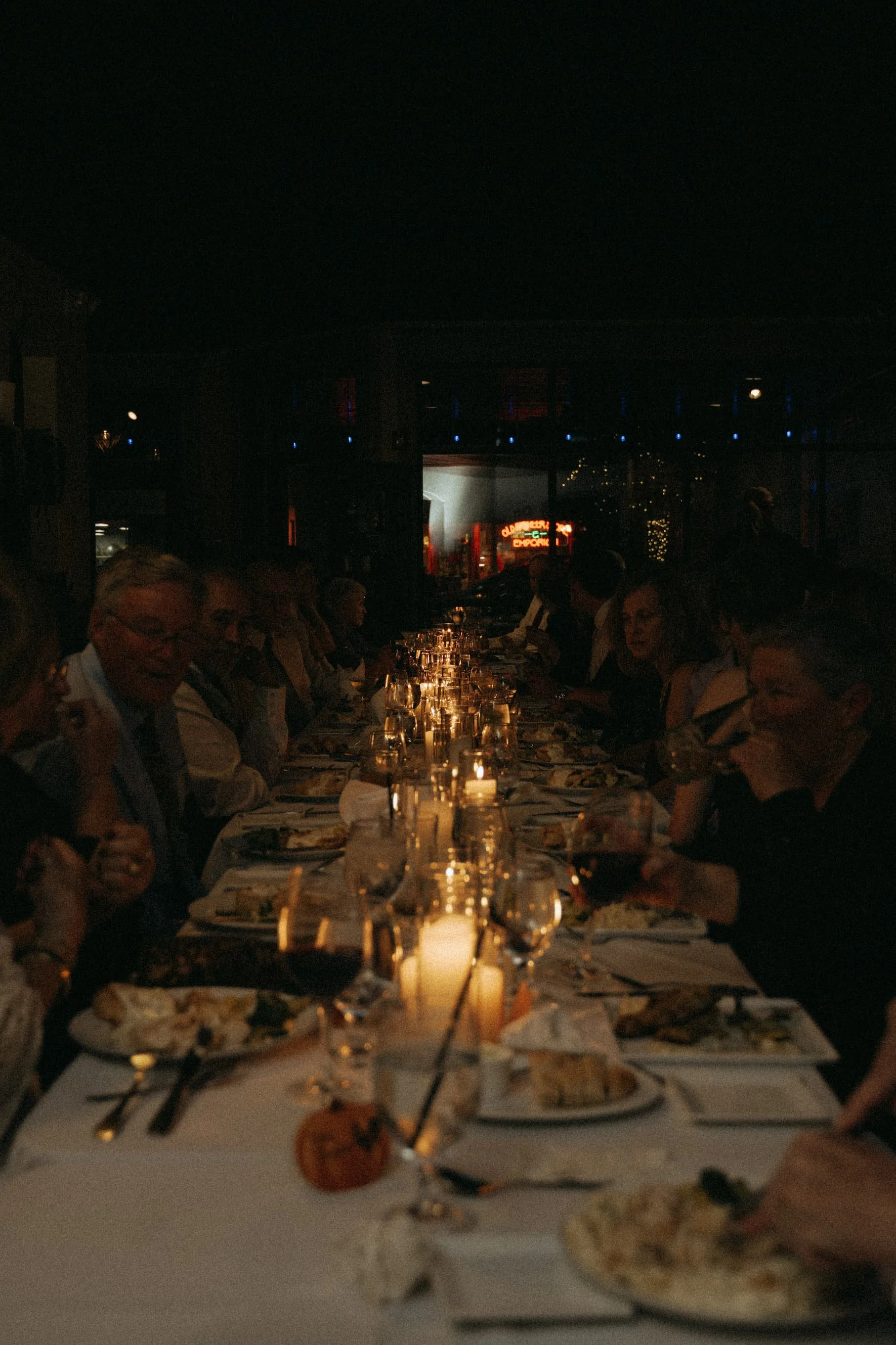 People dining at a long candlelit table inside a restaurant at night.