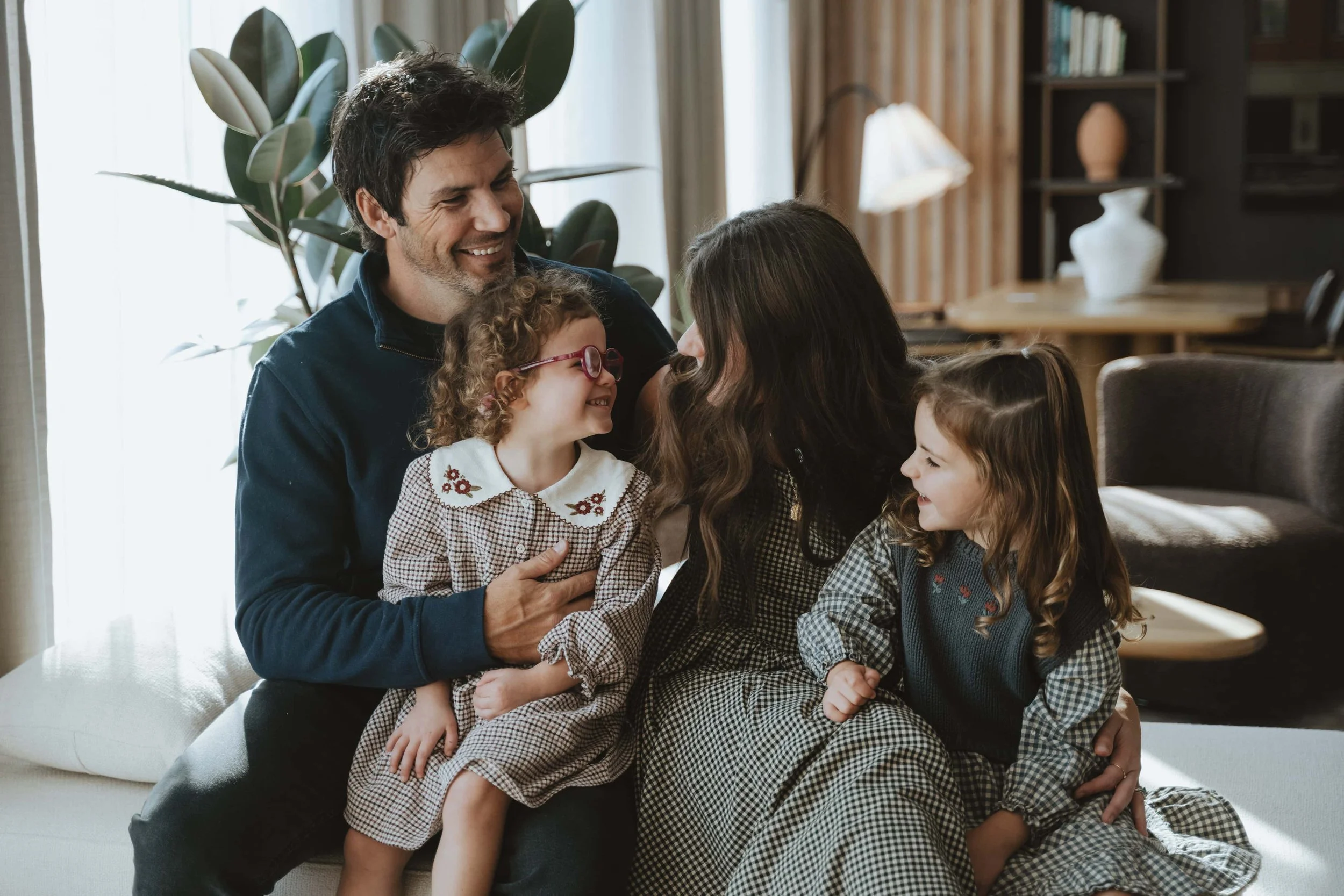 A family of five sitting together in a cozy living room, smiling and laughing, with two young girls and their parents. Family session in grand rapids michigan