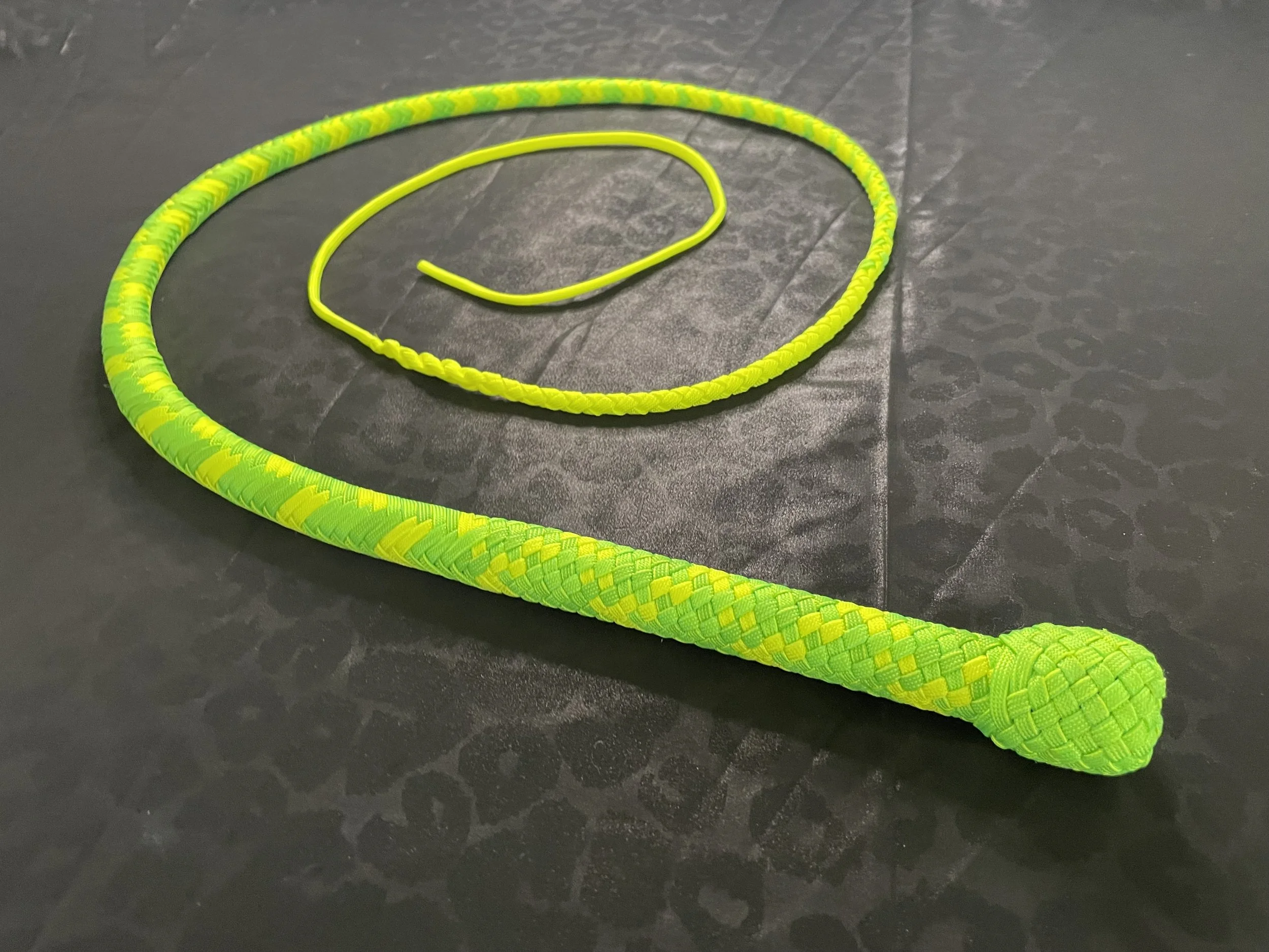 Bright yellow and green jump rope with braided handles on a black textured surface.