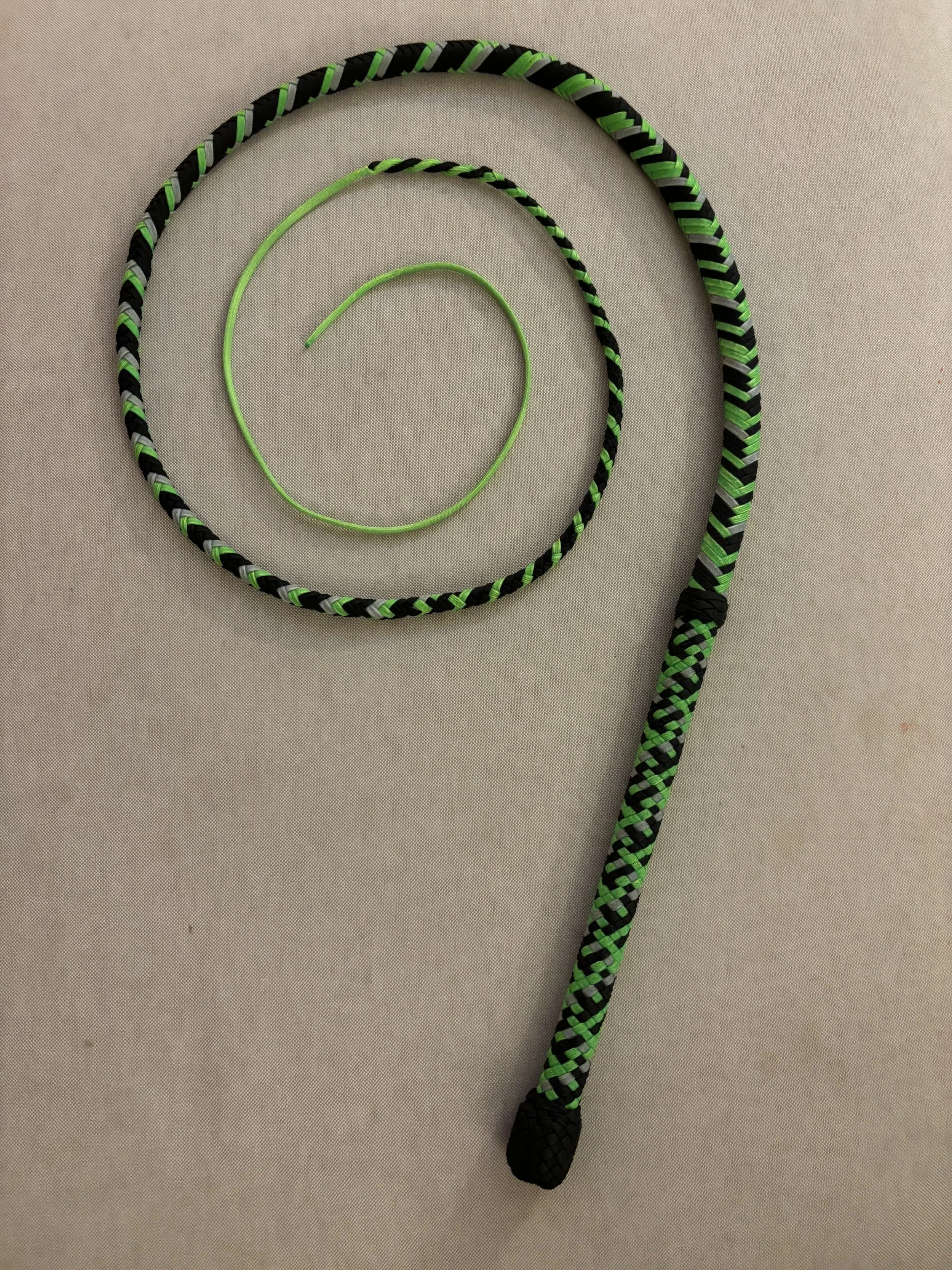 Colorful jump rope with black, green, and white braided handle and a green cable, placed on a gray surface.