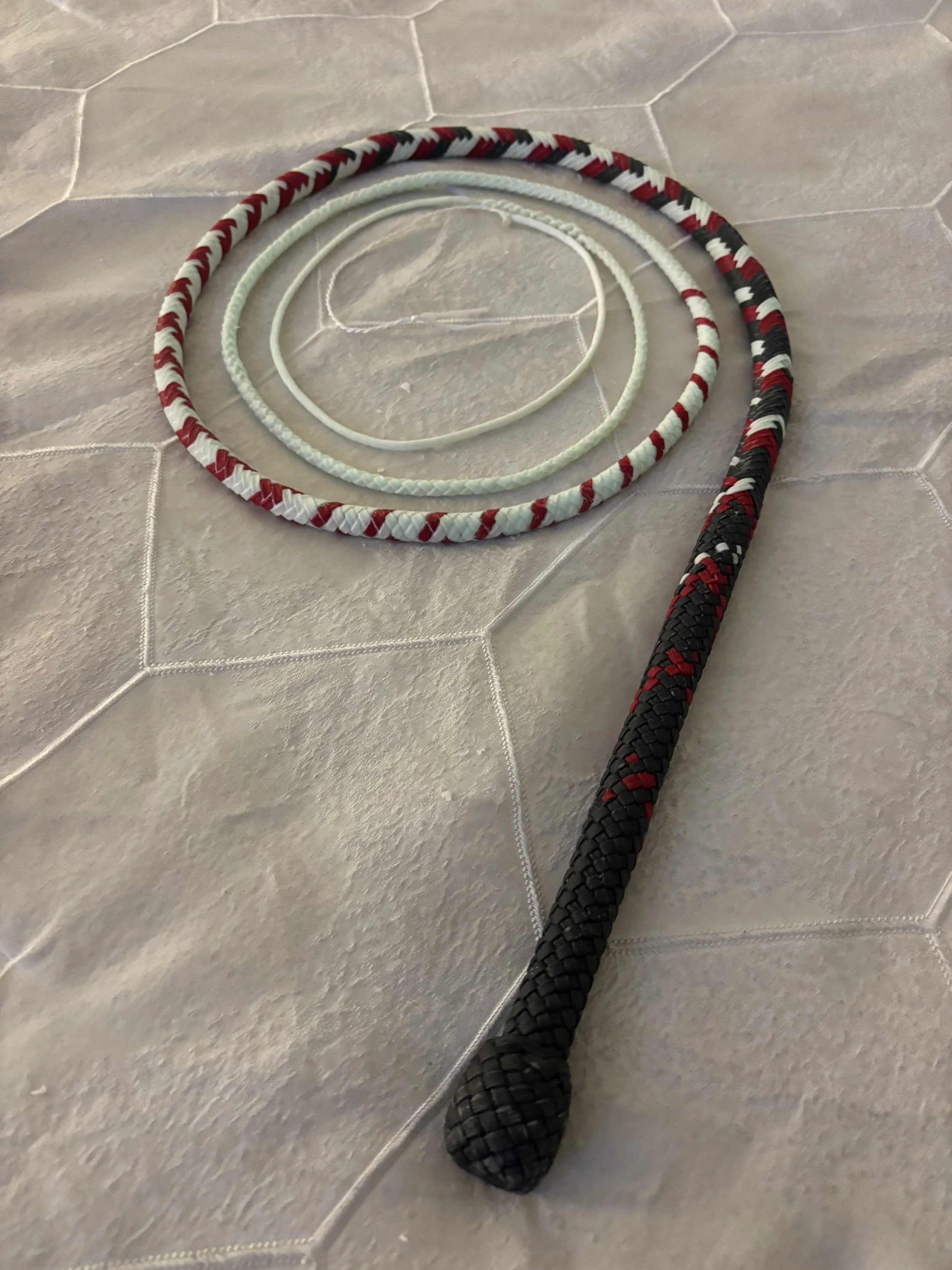 Three jump ropes with coiled handles on a tiled floor, one black with red accents, one white, and one white with red and black patterns.