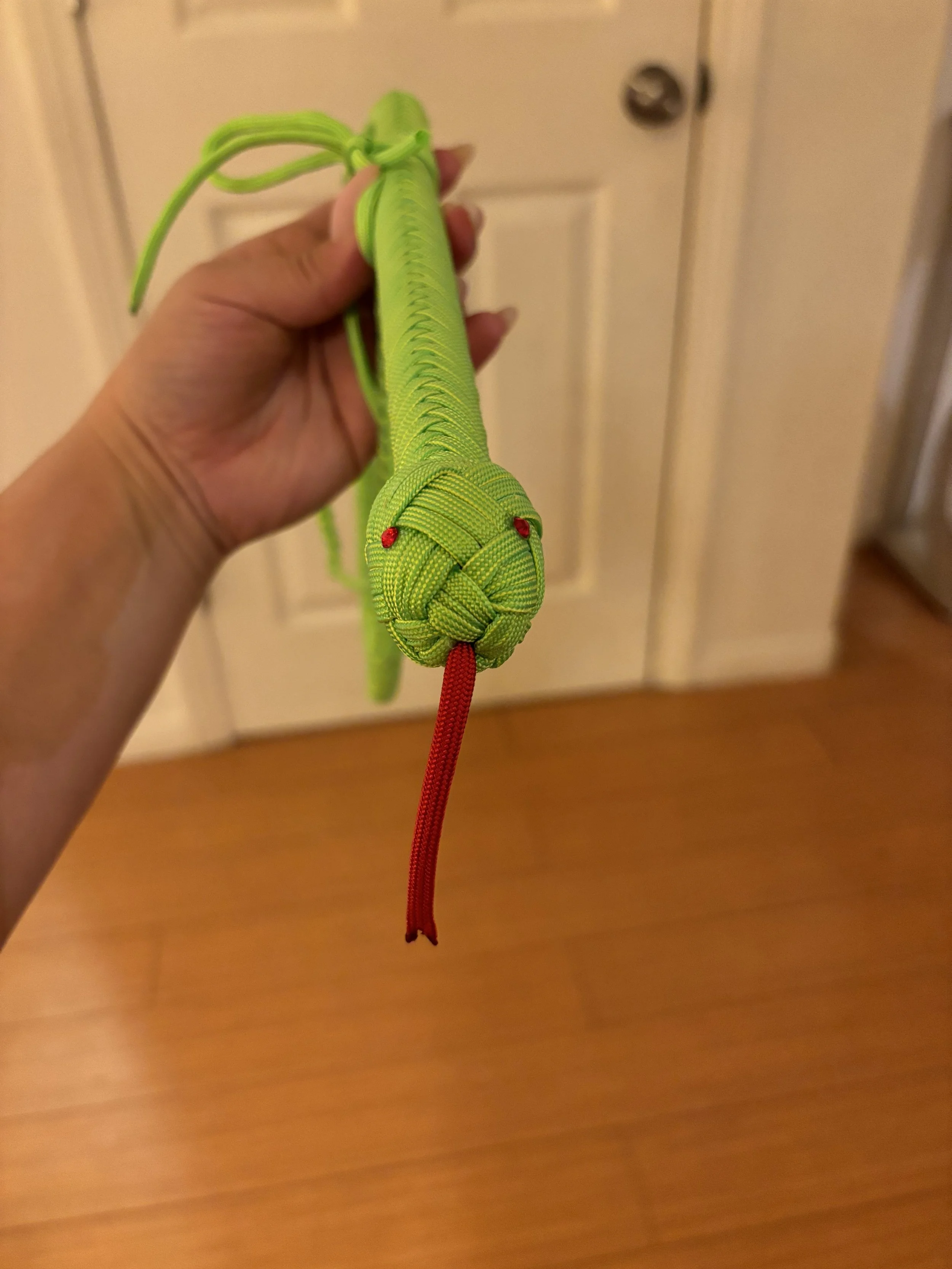 Hand holding a green plastic toy snake with red eyes and a red tongue, shaped from woven material.