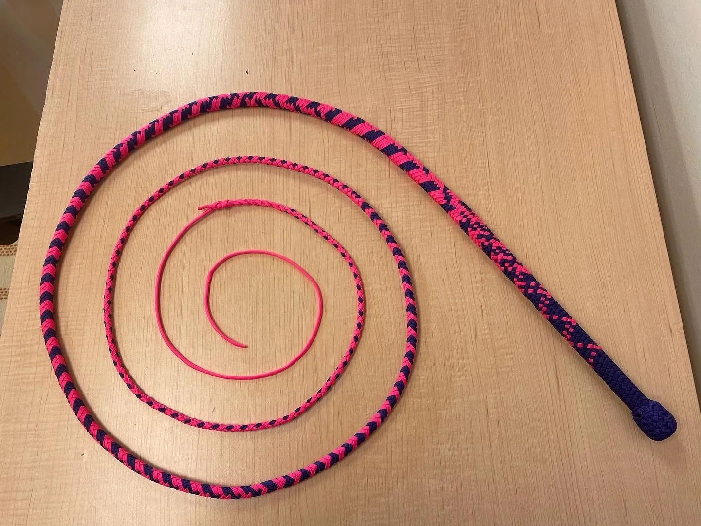 Set of four pink and navy braided jump ropes arranged in a spiral pattern on a wooden surface.