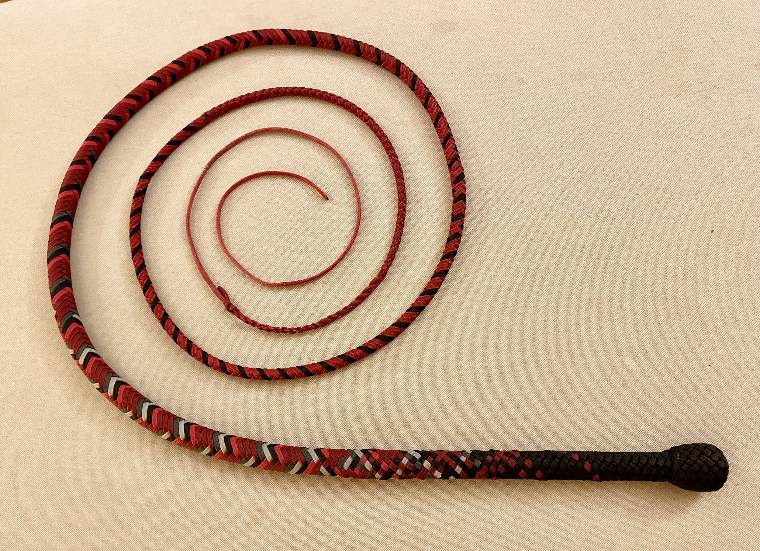 Four red and black braided climbing or lanyard ropes of varying lengths arranged in a spiral on a beige background.