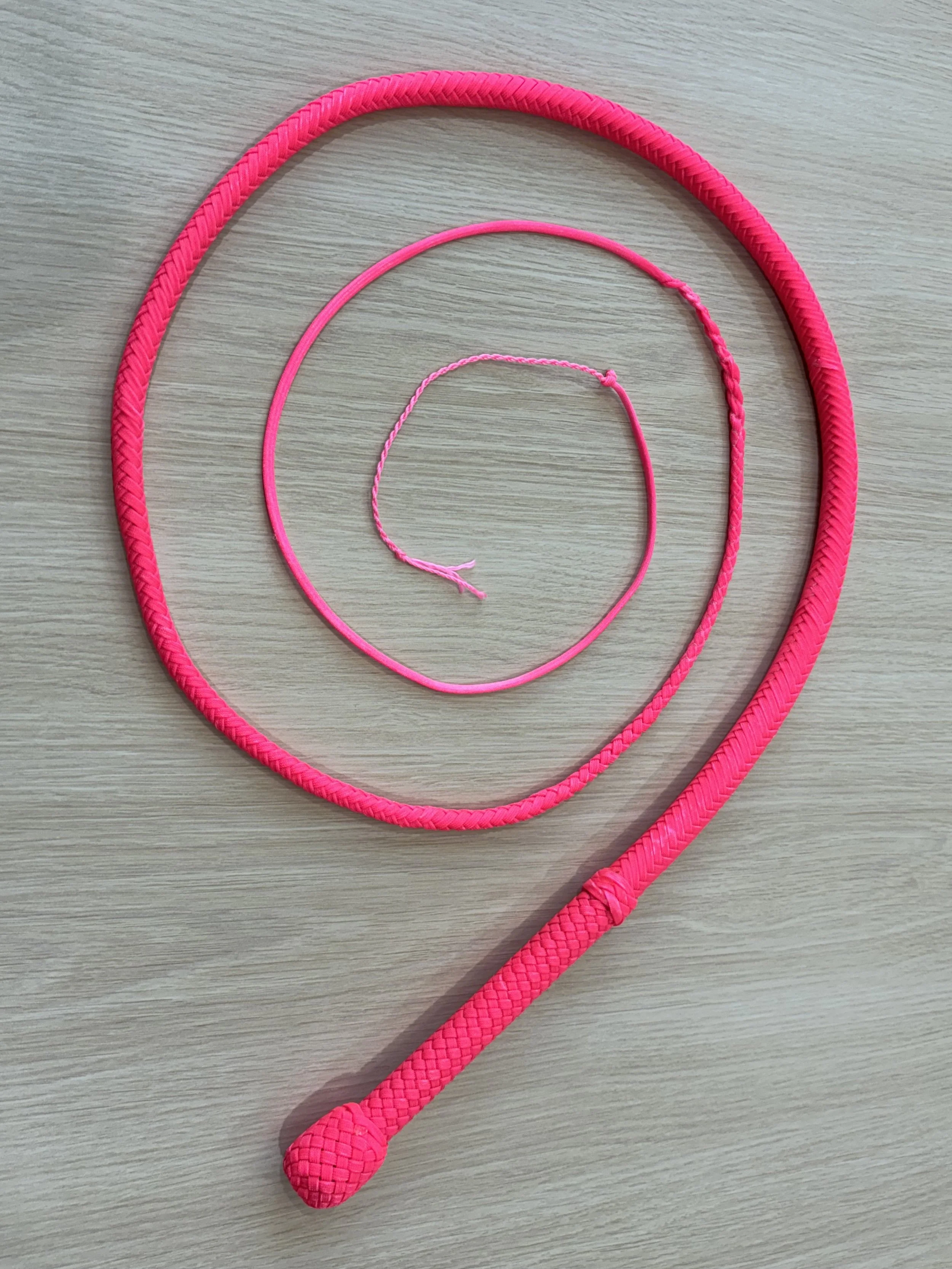 Three pink jump ropes of varying sizes laid out in a spiral on a light wooden surface.