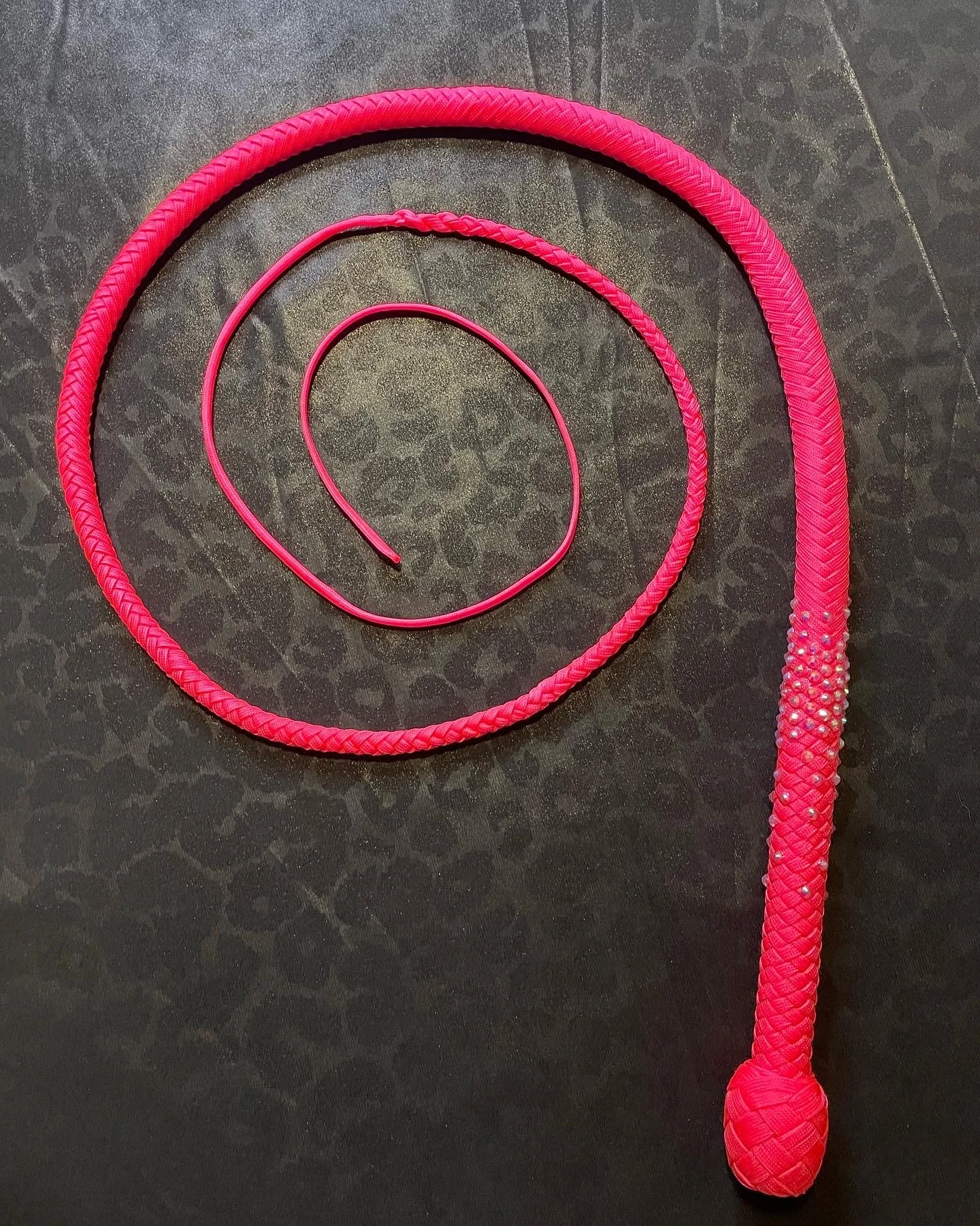 Pink braided whip with a ball at the end and a matching thin pink whip on a dark textured surface.