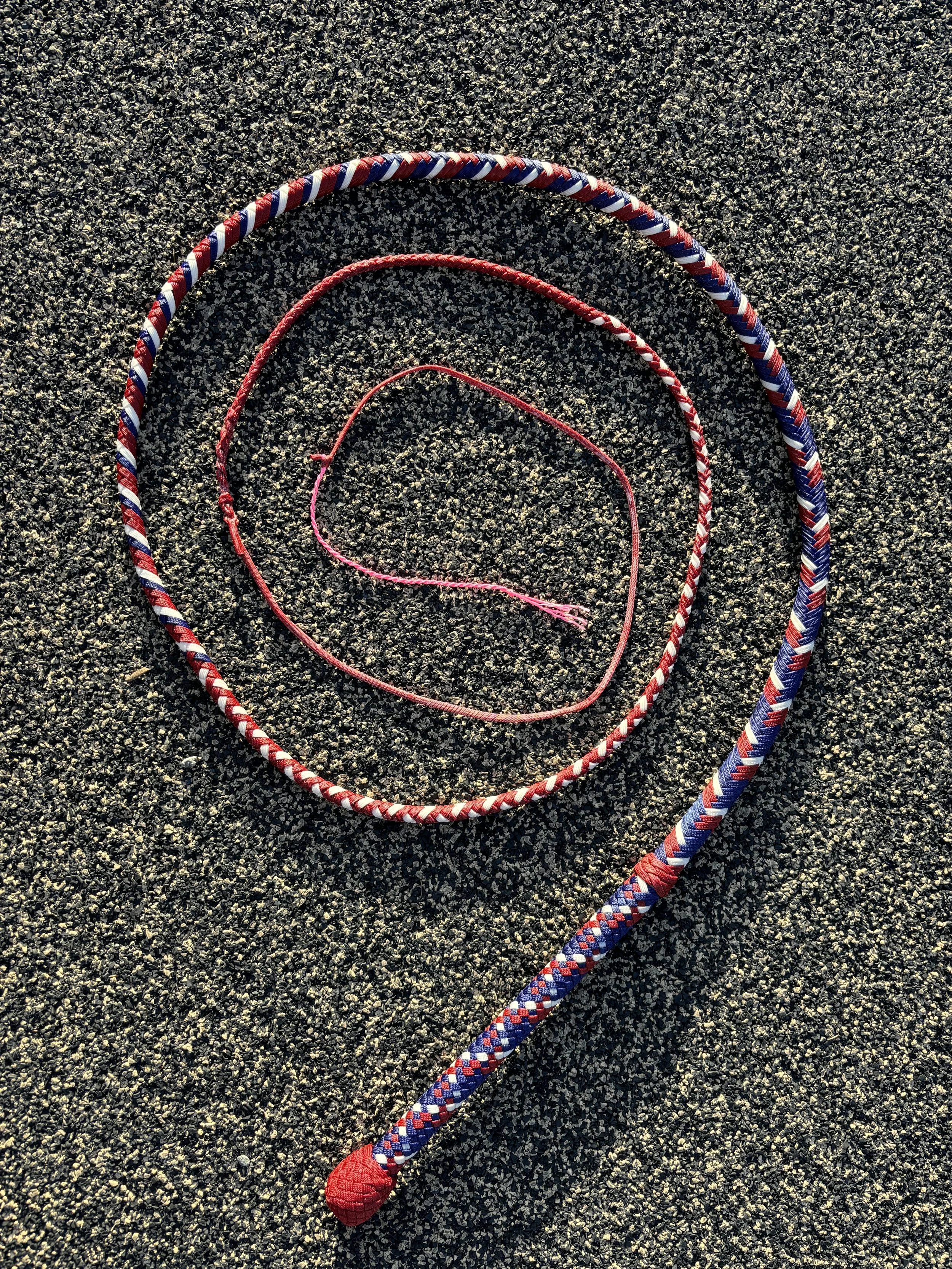 Three jump ropes of different sizes and colors lying on a textured outdoor surface.