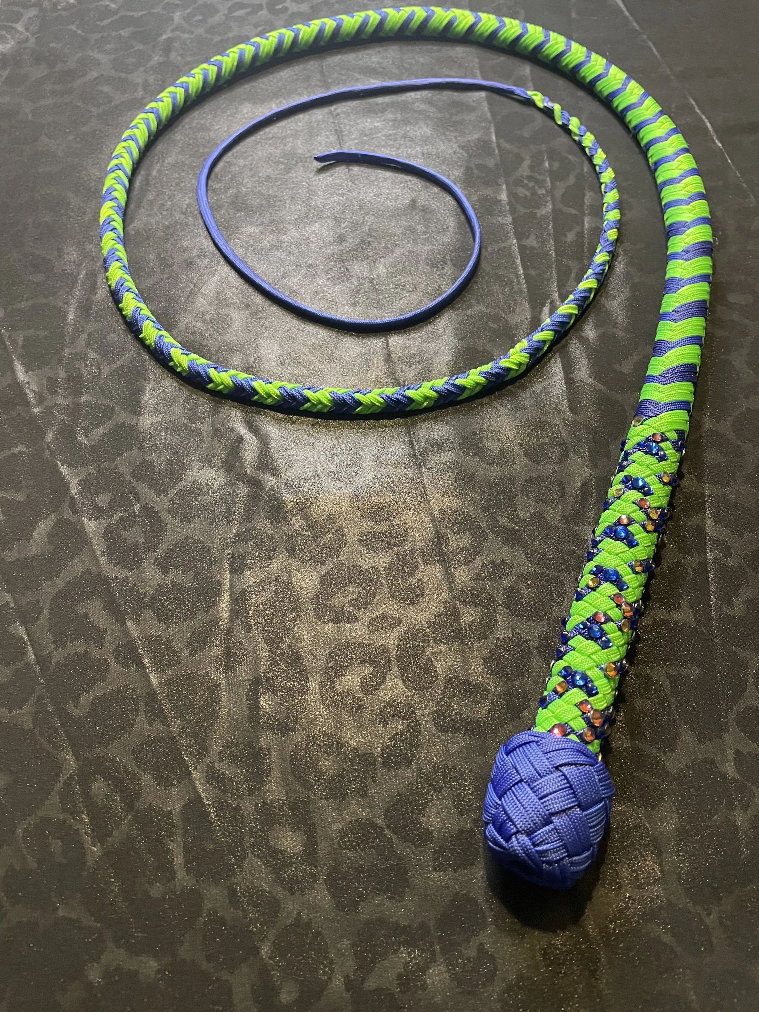 Colorful braided dog toy with blue pom-pom on the end, lying on a dark textured surface.