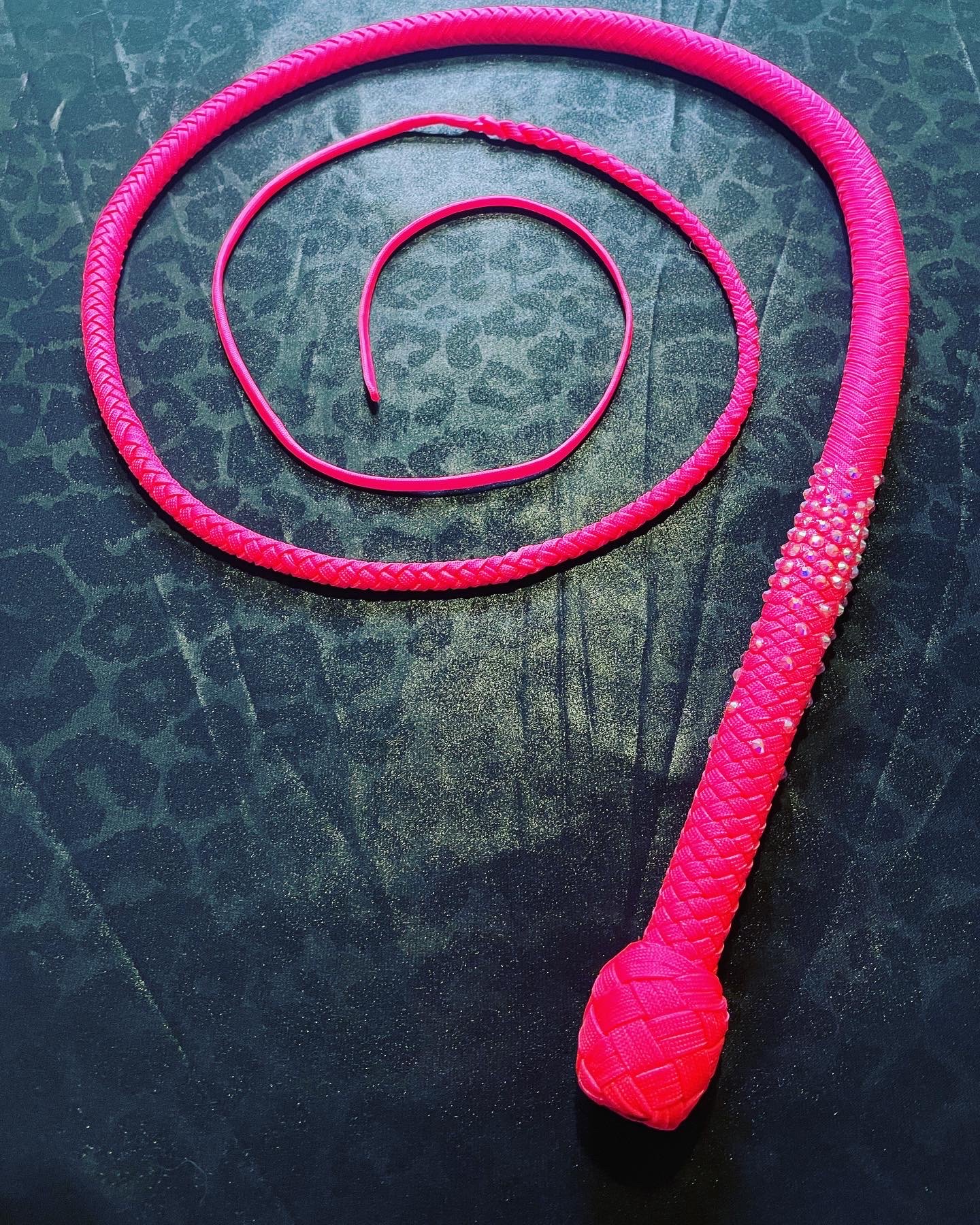 Three pink jewelry pieces on a dark surface, including a large braided necklace, a smaller thin bangle, and a thick snake-shaped ring.