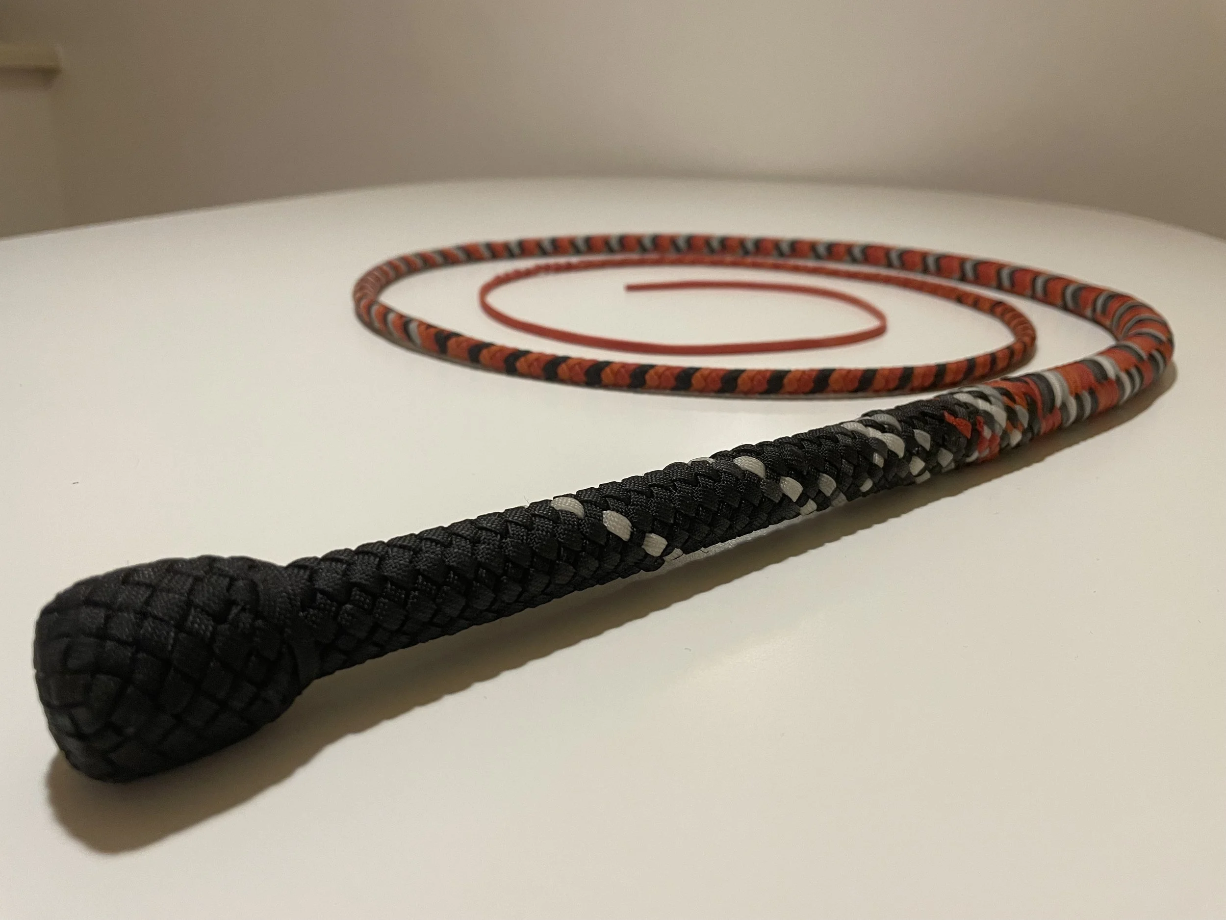 A black braided rope with a rounded handle, and a red and black coiled rope, both on a white surface.