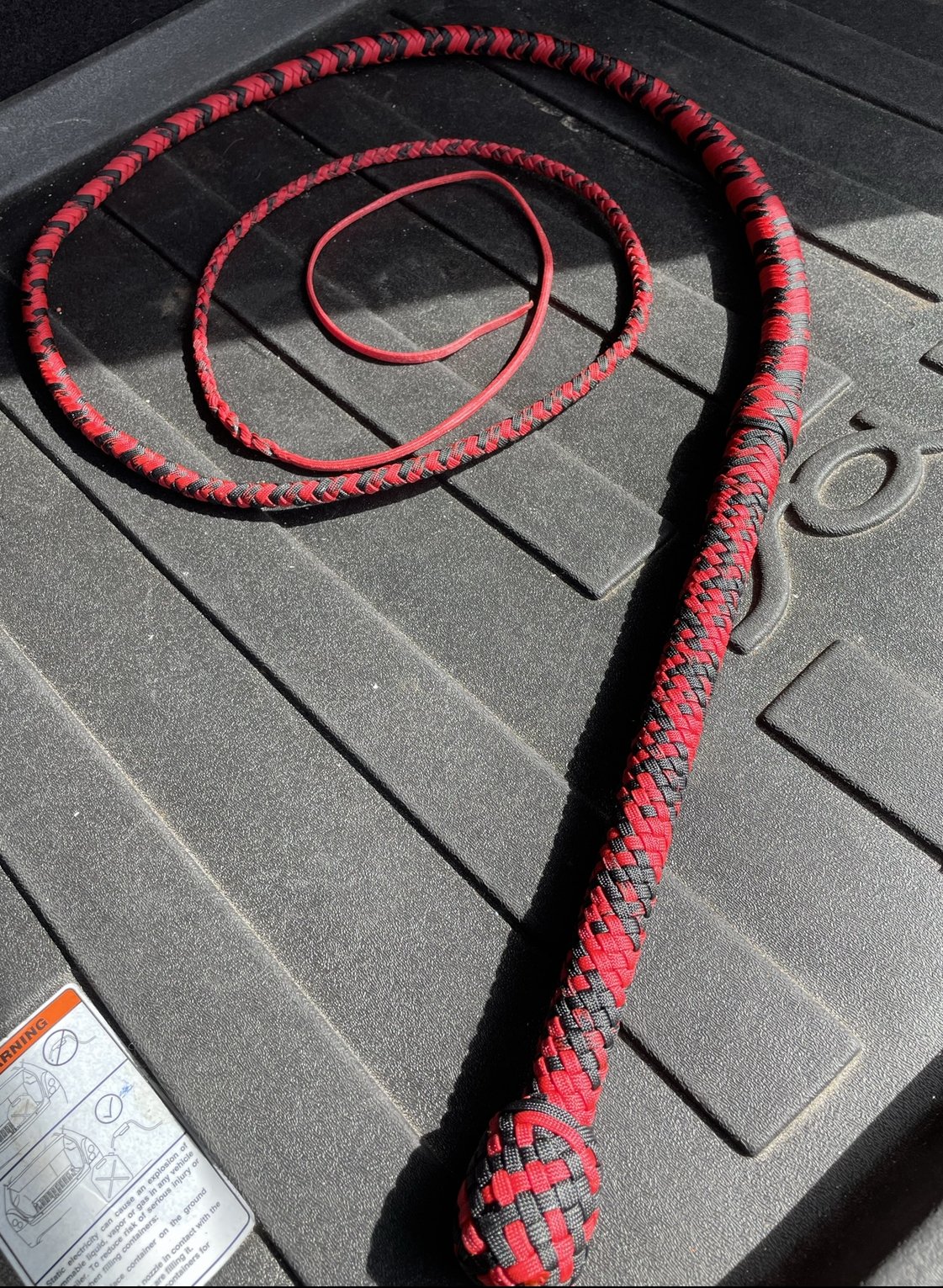 A black and red woven rope and a thin red cord on a black rubber surface.