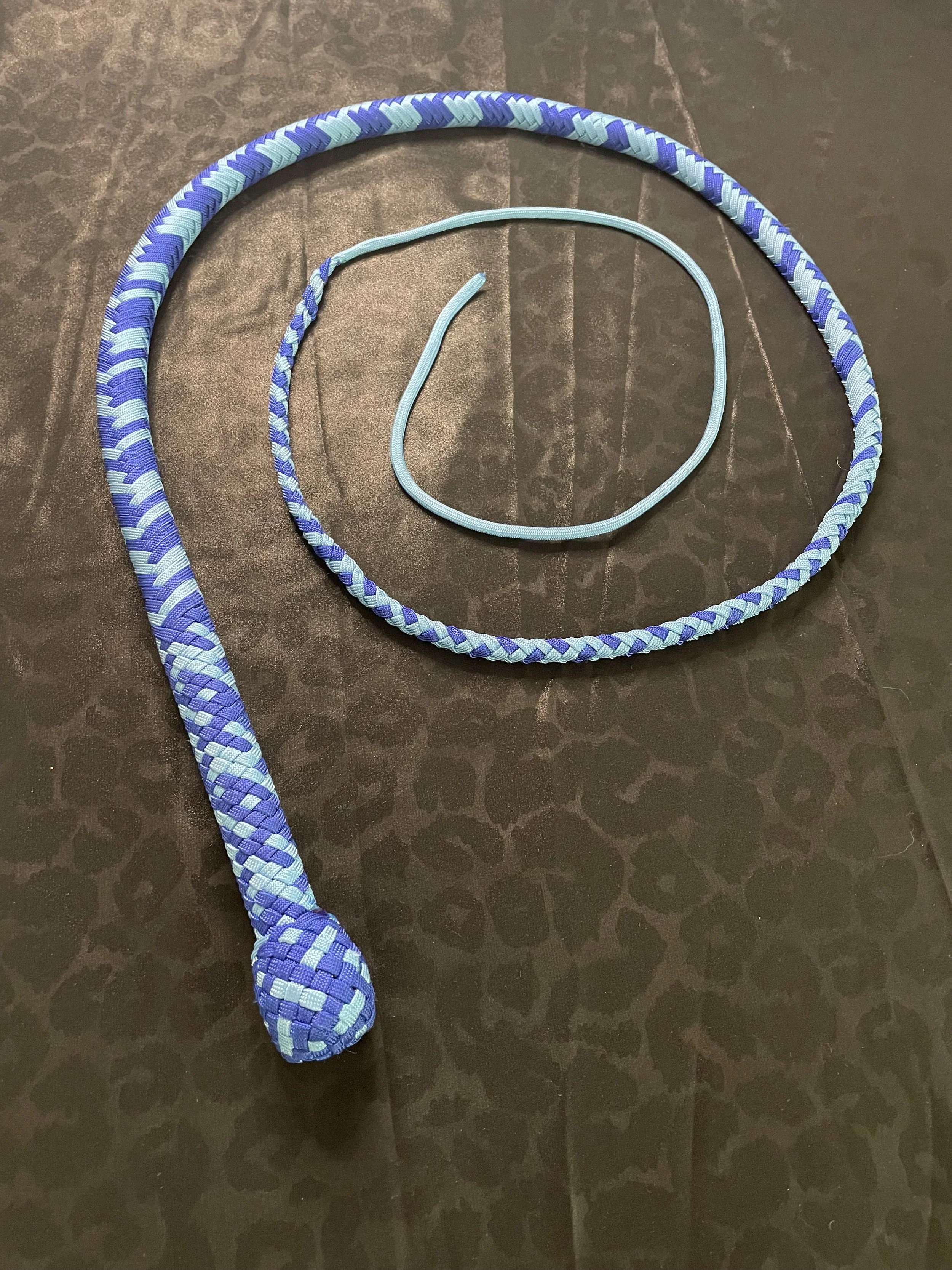 A blue and light blue woven rope with a knotted end, a blue shoelace, and a light blue elastic band on a dark textured surface.