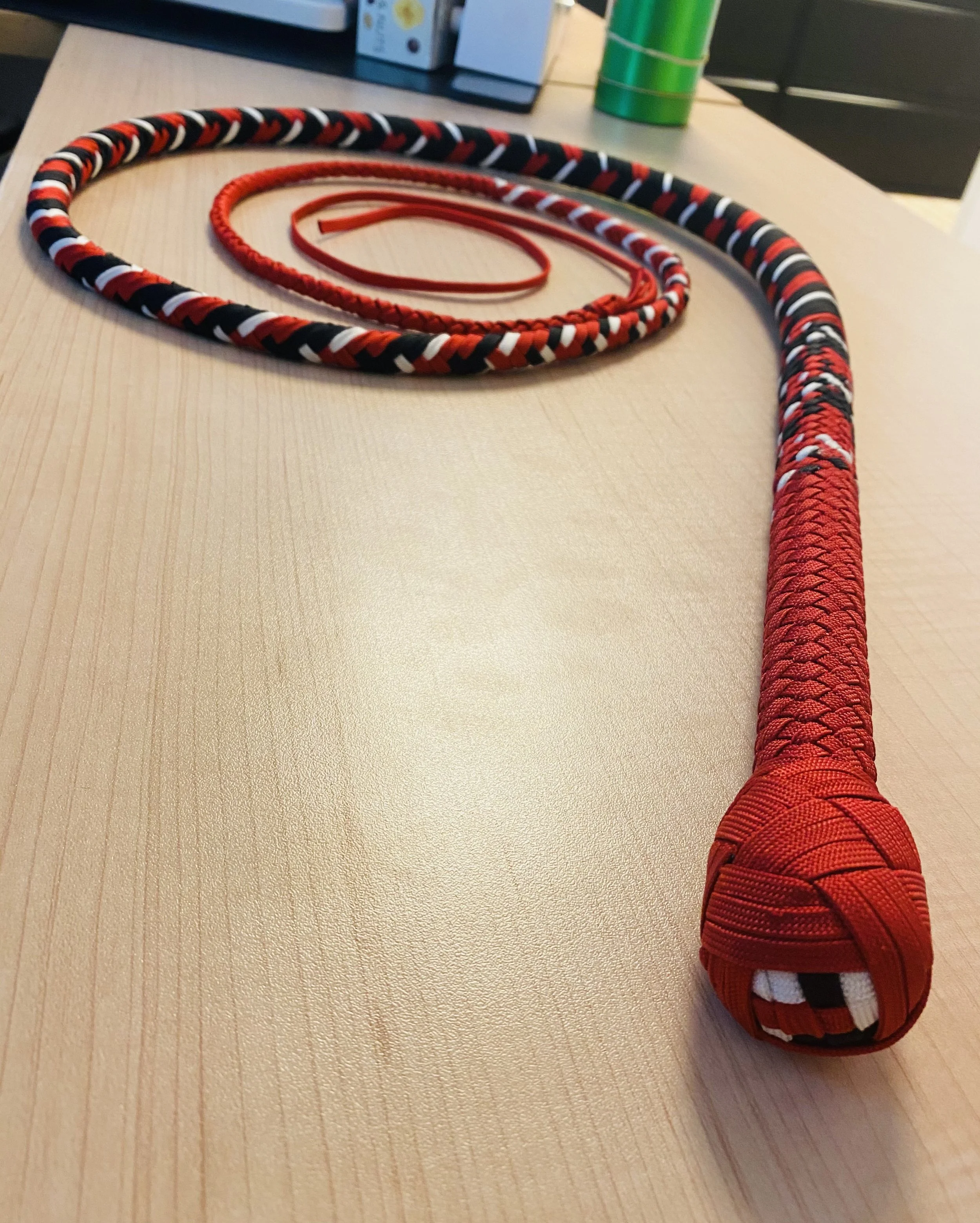 A long, woven red, black, and white rope with a knot at one end, lying on a wooden surface.