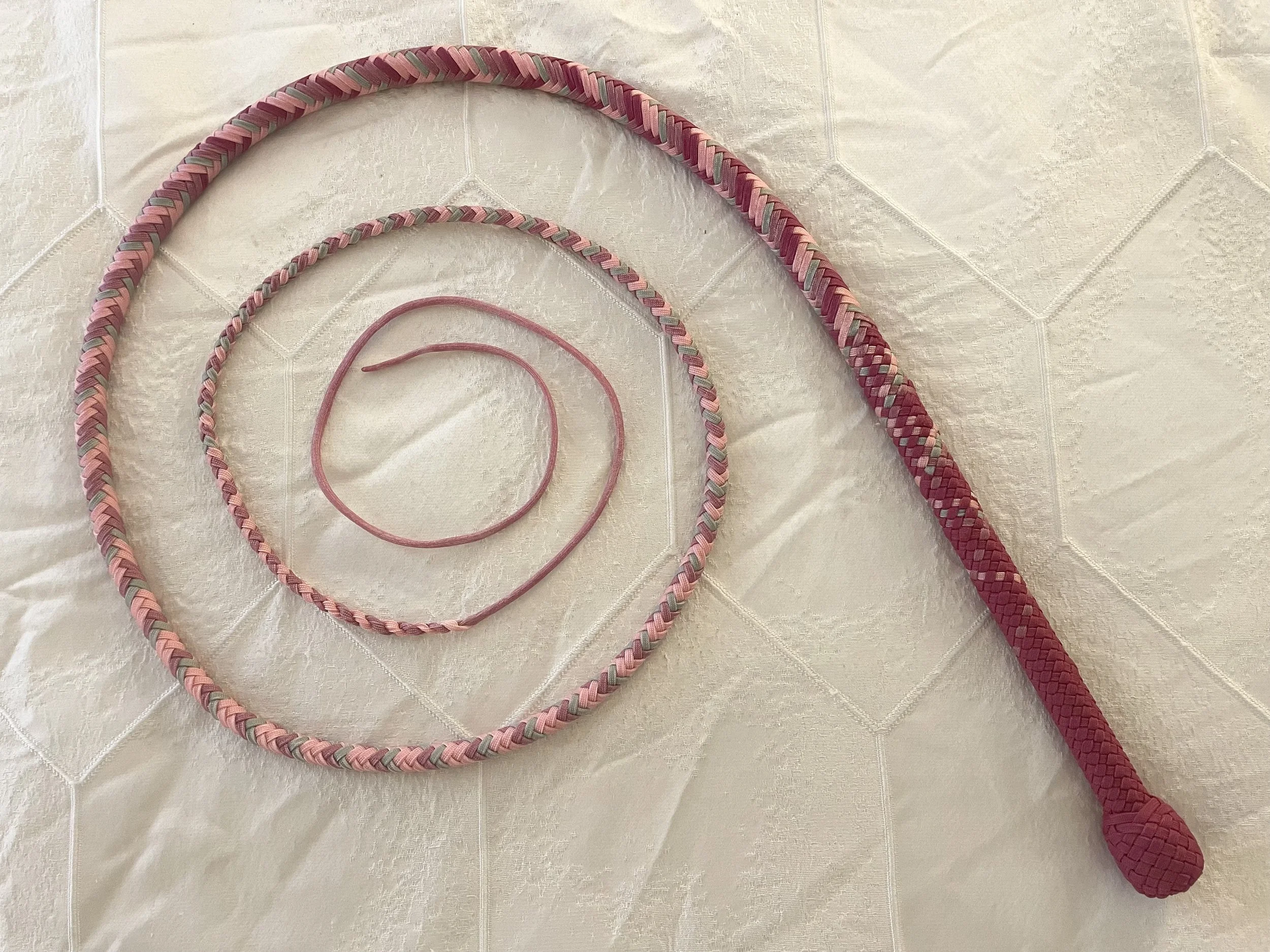 Three pink and gray braided jump ropes of varying lengths, with a textured handle, lying on a cream-colored tiled surface.