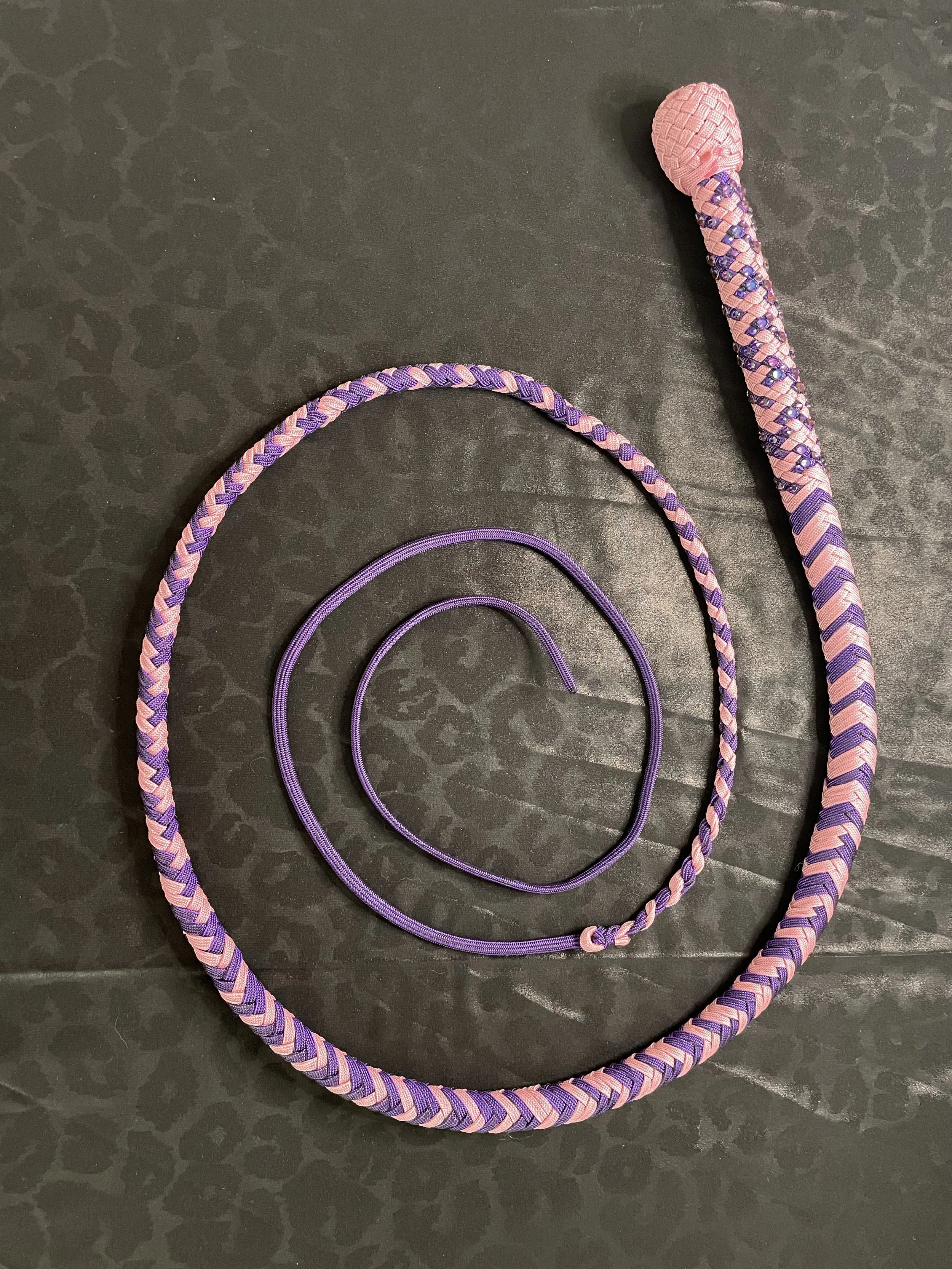 A pink and purple braided dog leash with a pink handle, along with a purple collar, on a dark textured surface.