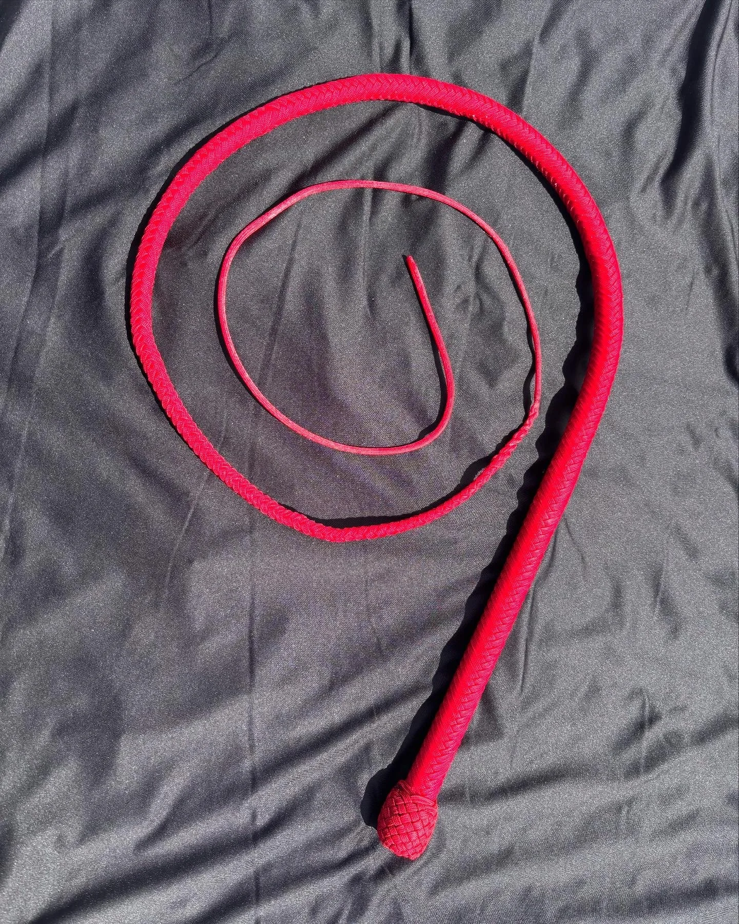 Red jump rope with a textured handle on a black fabric background.