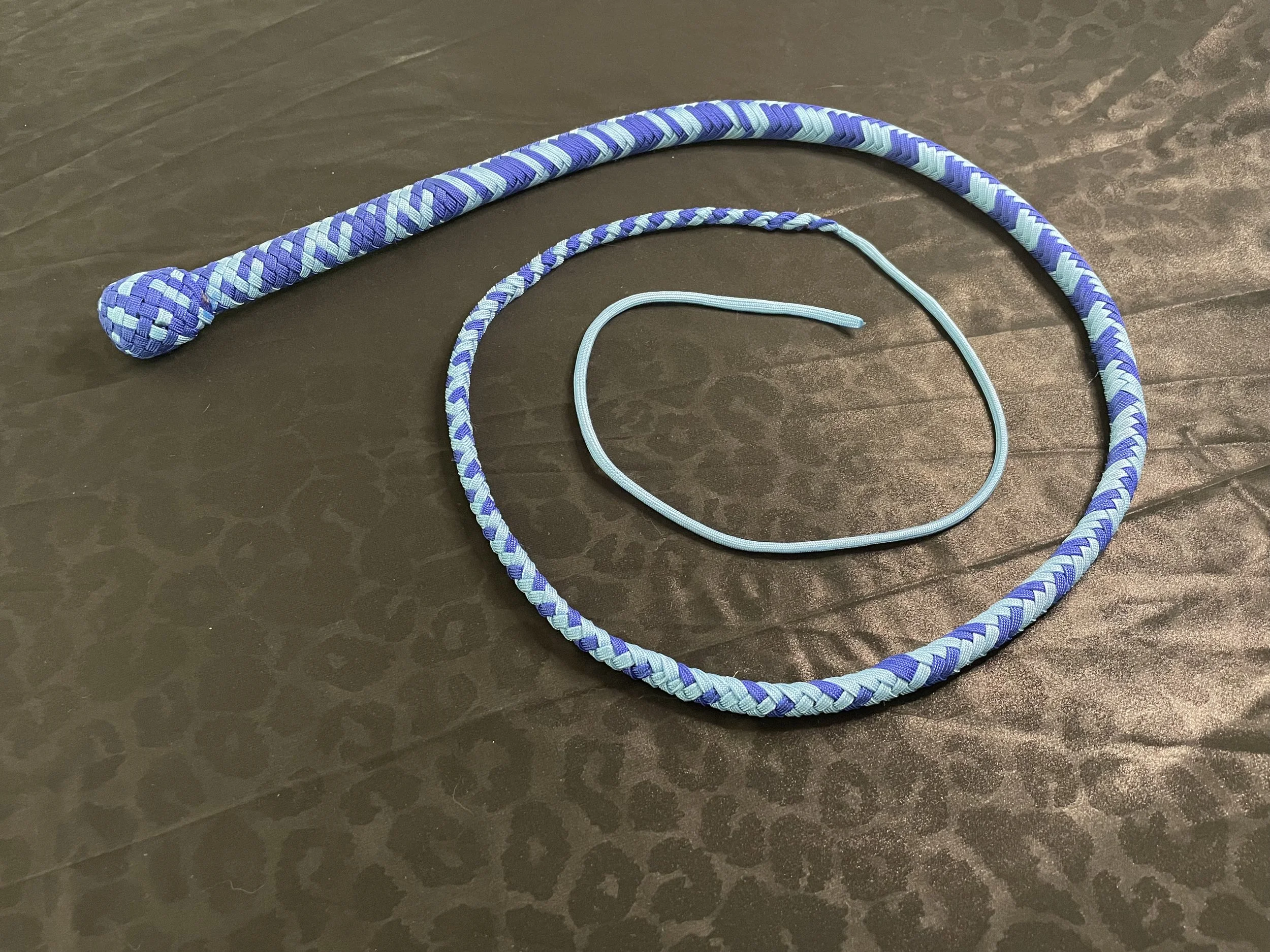A blue braided jump rope with a looped cord lying on a dark, textured surface.