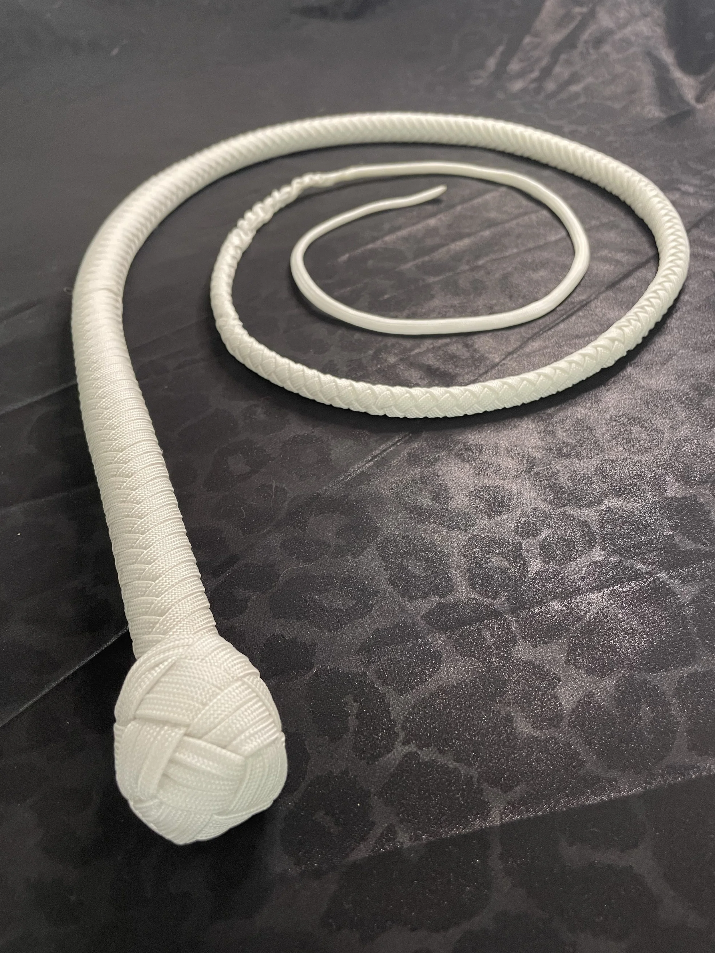 A white braided extension cord with a round plug end, lying on a dark textured surface.