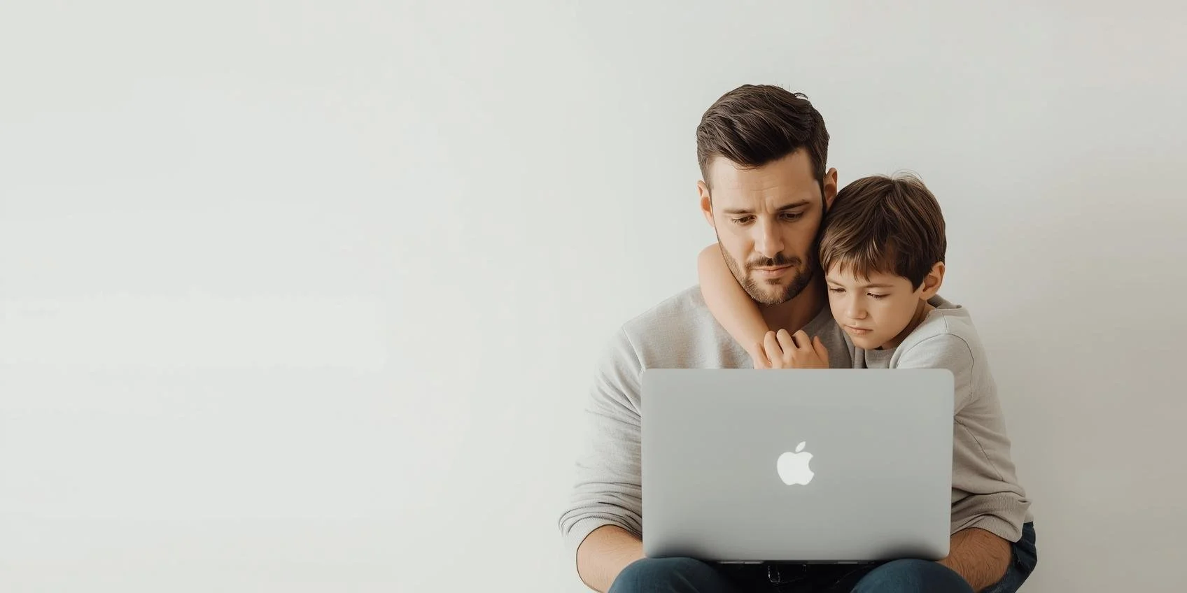 A father is angry as he has to do work on his laptop while his child hugs him.