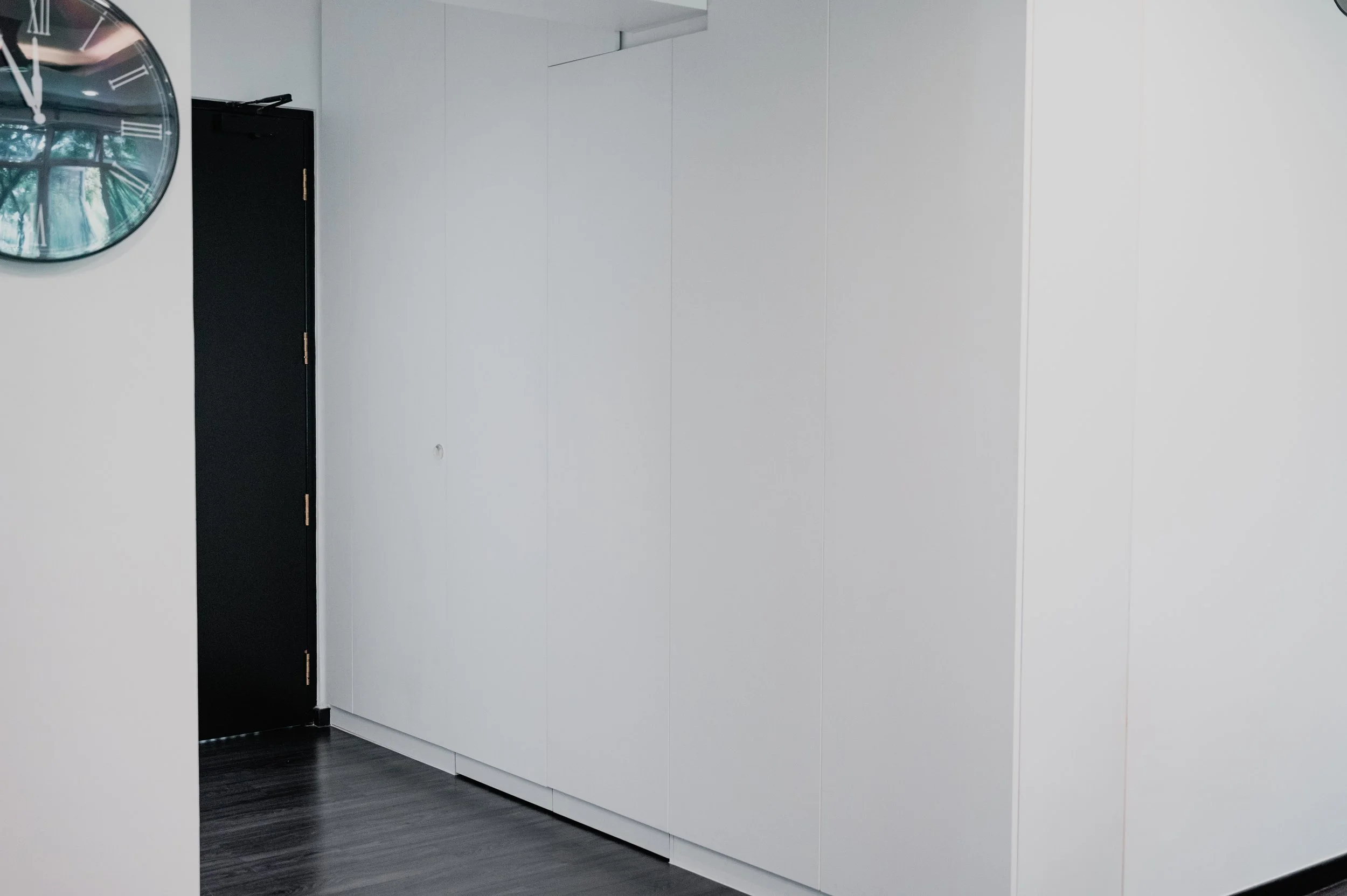 Modern interior with white wall, black door, and large wall clock showing time.