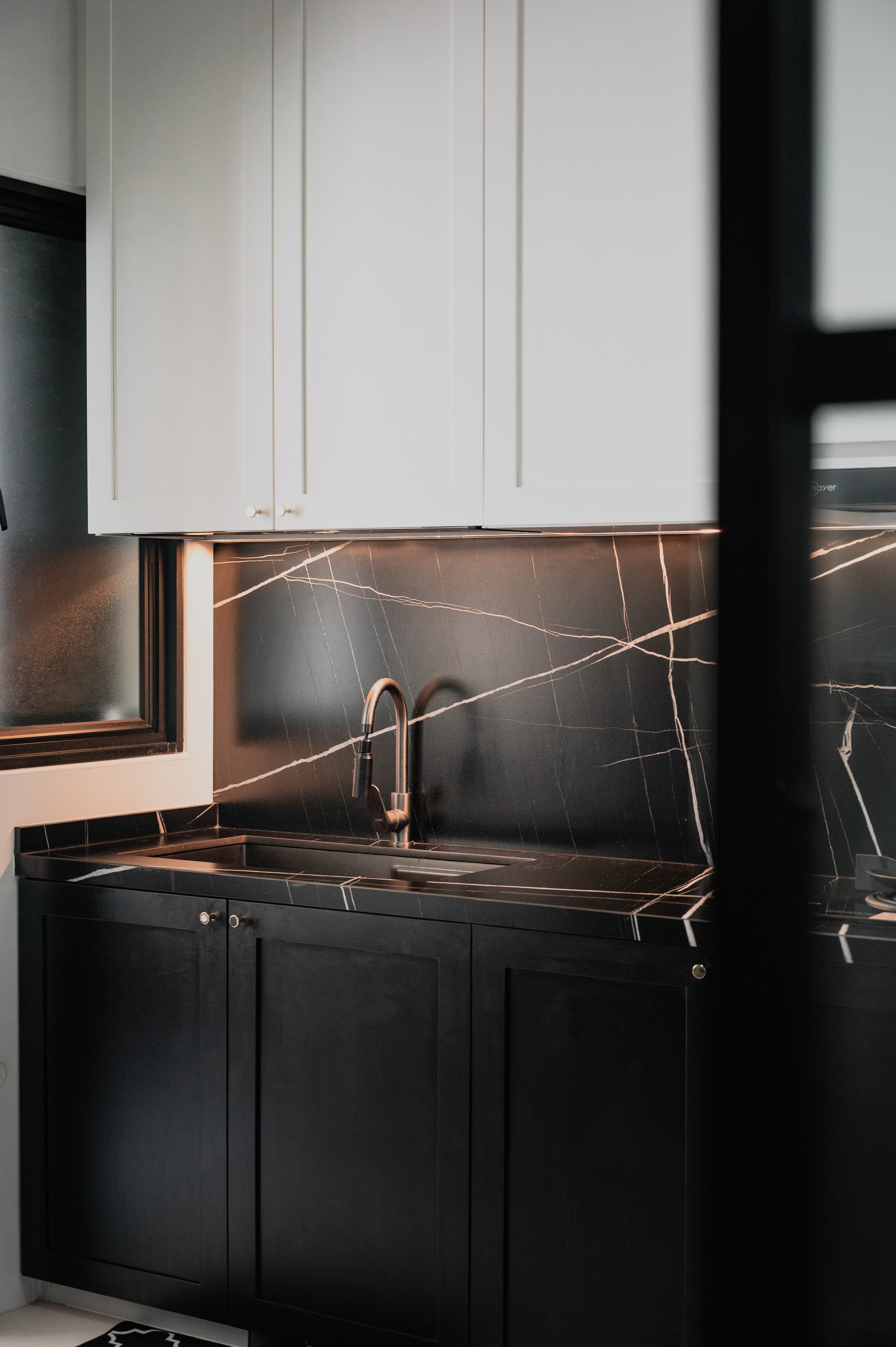 Modern kitchen with black marble countertops and backsplash, black lower cabinets, white upper cabinets, and a stainless steel faucet over a sink.
