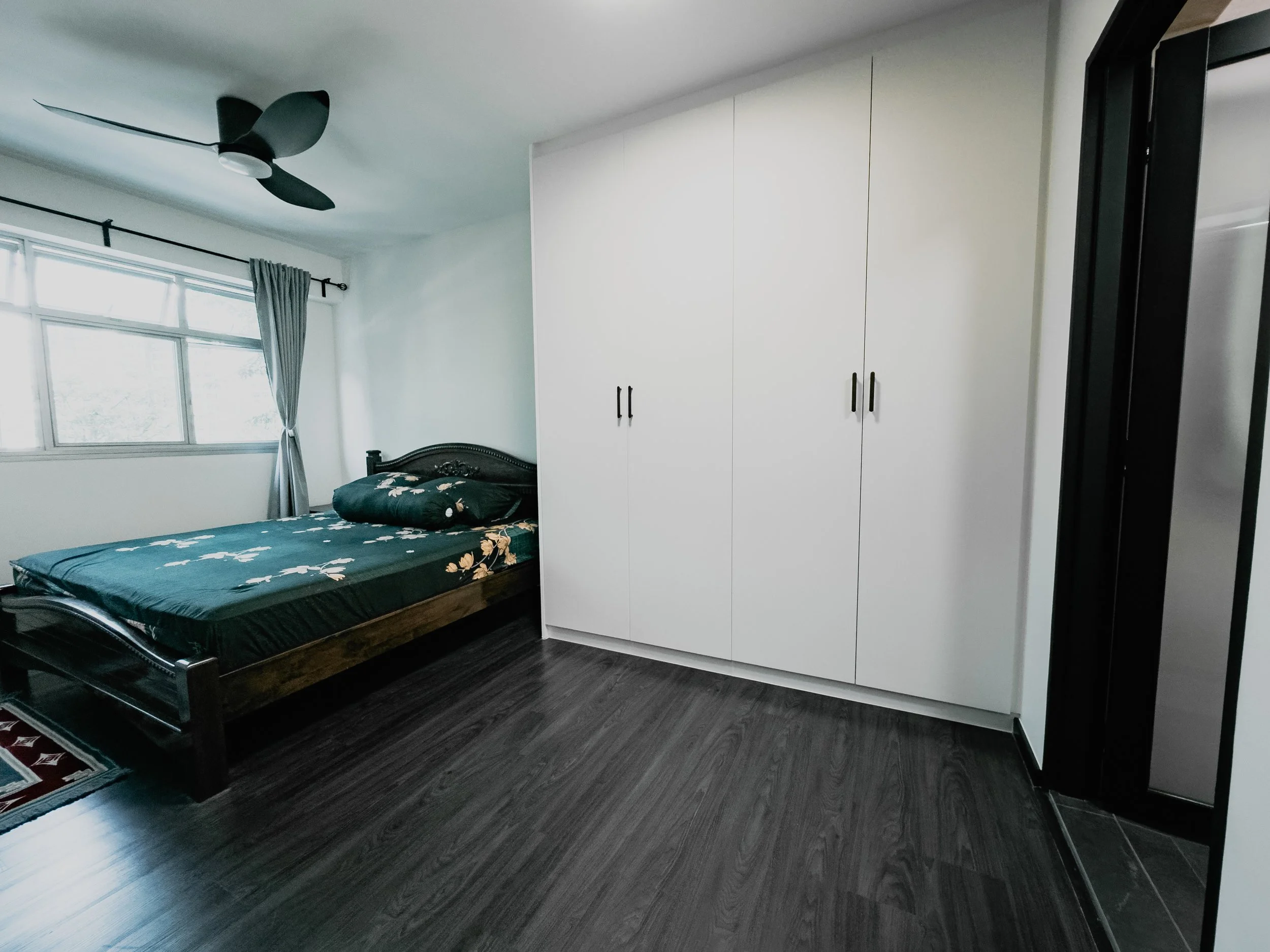 Bedroom with a bed, a window with curtains, a white wardrobe, and a ceiling fan.