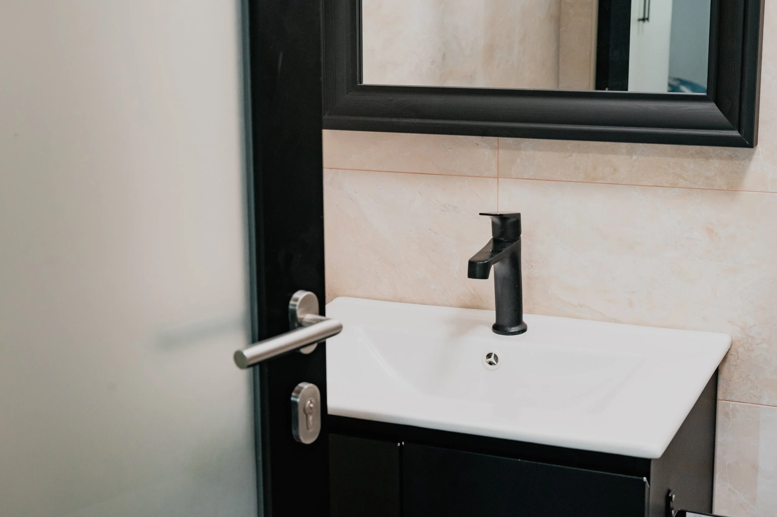 Bathroom sink with black faucet and mirror reflected in a partially opened door.