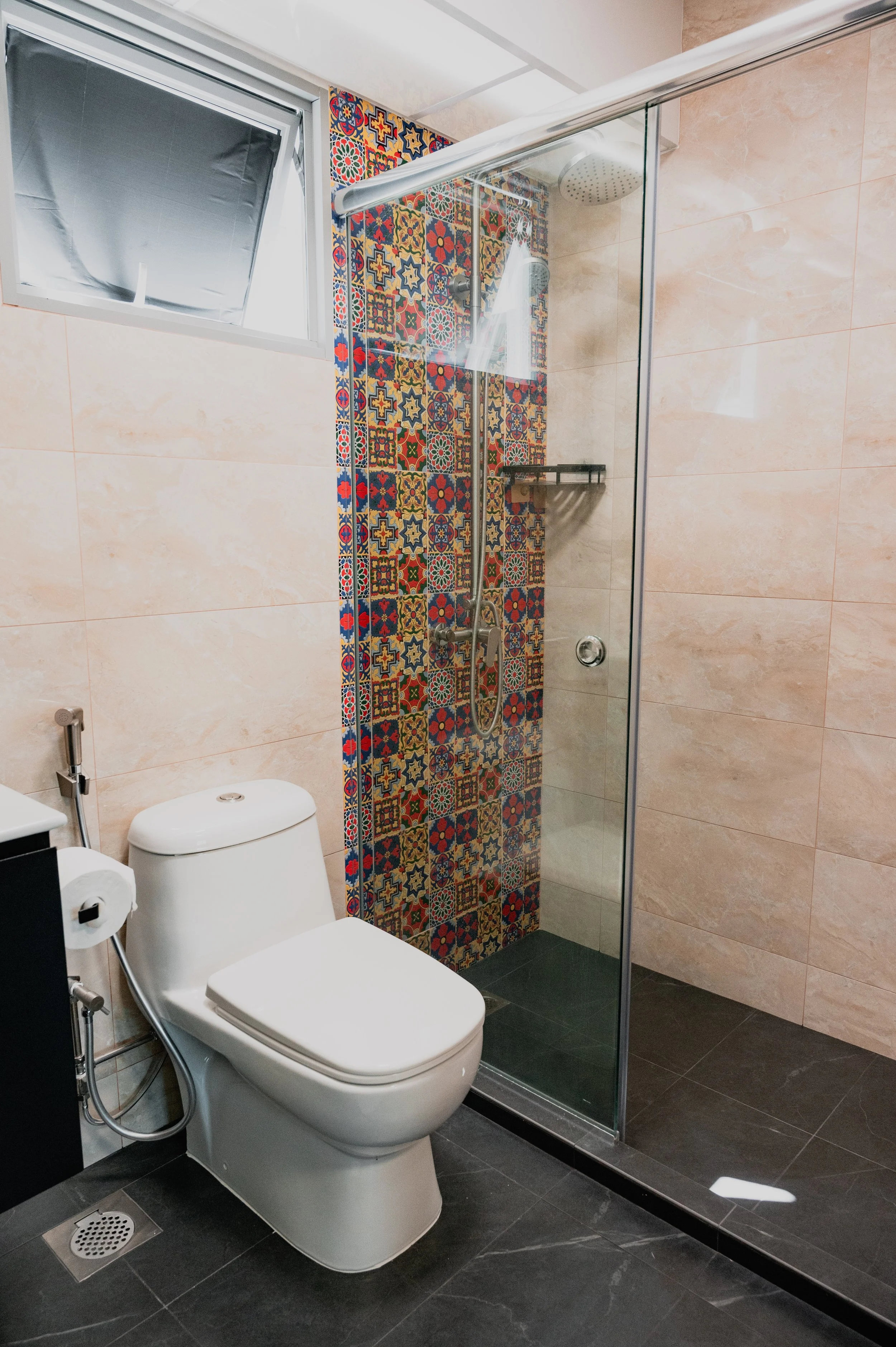 A modern bathroom with a white toilet, black floor tiles, and a shower area with colorful patterned tiles on the wall behind the showerhead.