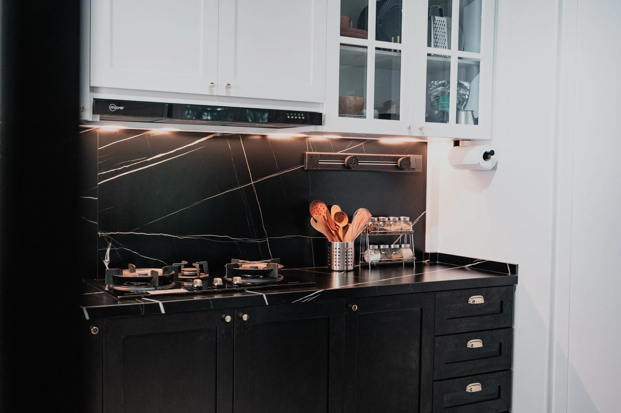 Modern kitchen with black marble backsplash and countertop, white cabinets, and black cabinetry with drawers.