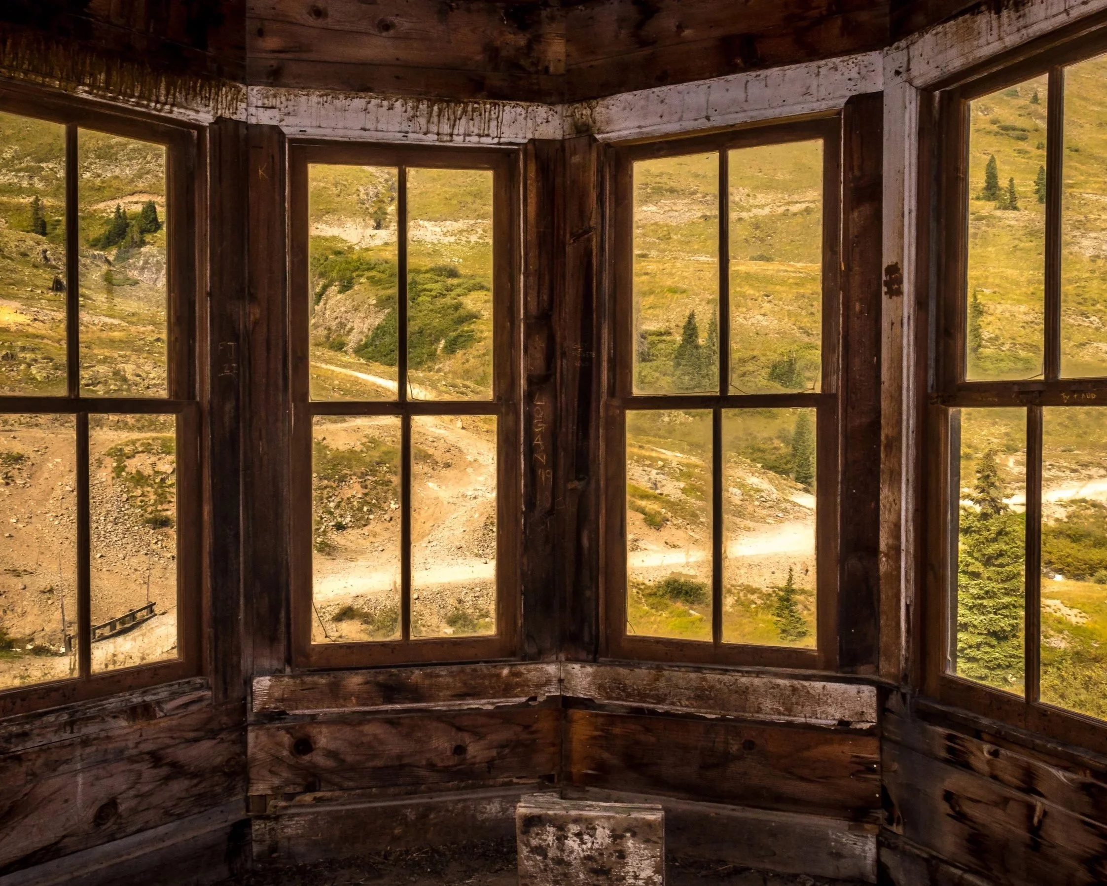 Interior view of a rustic alpine hut with weathered wood, simple structure, and light framing the surrounding landscape.