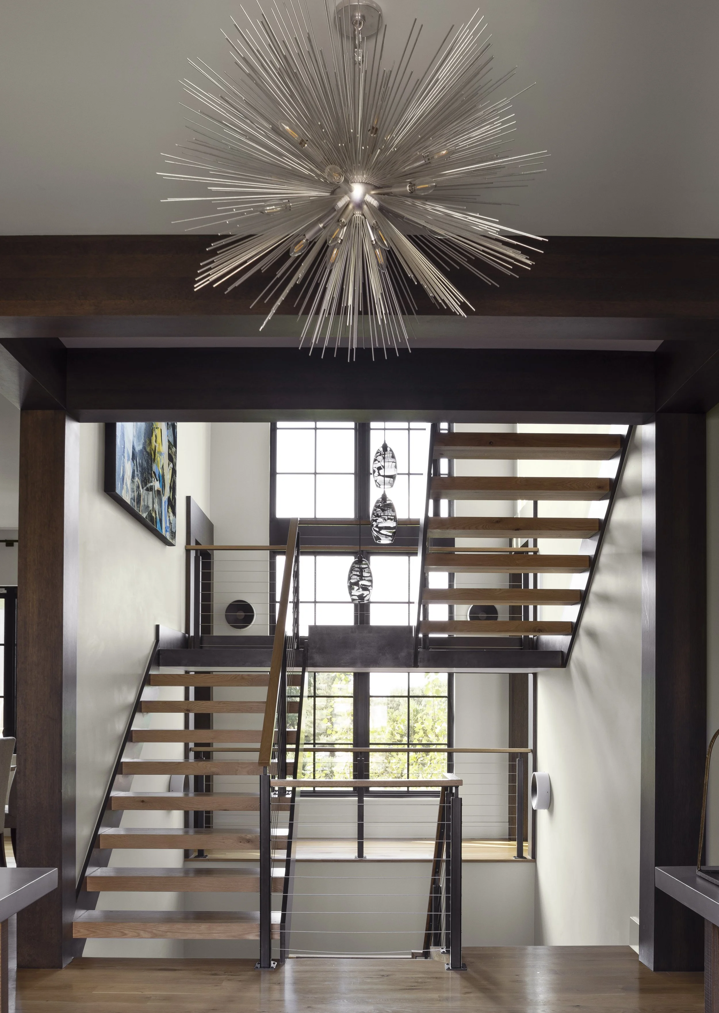 Sculptural chandelier illuminating a modern staircase with wood, glass and metal details.