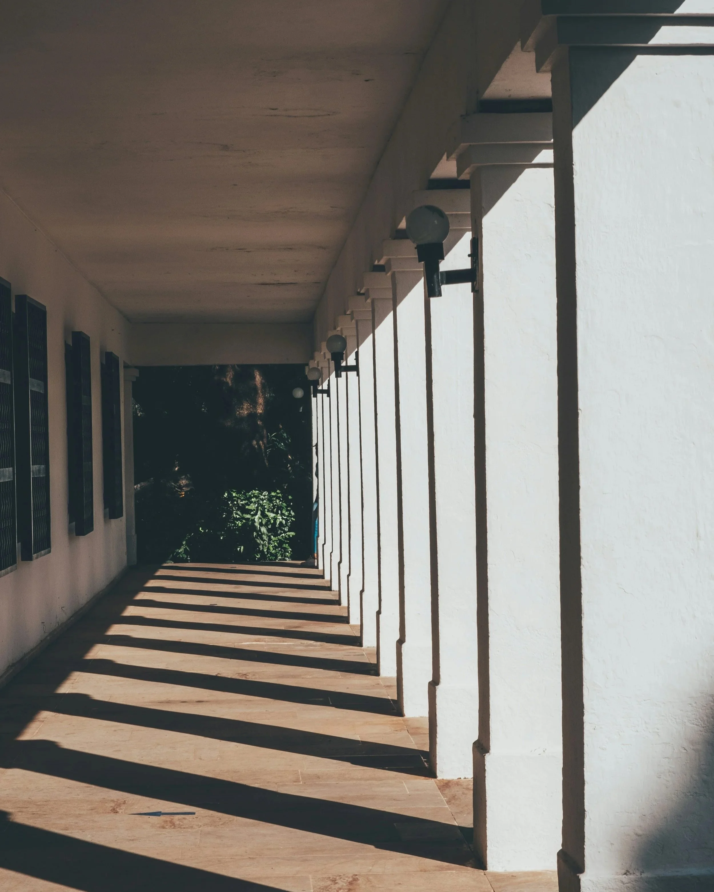 Architectural corridor with repeating columns and soft natural light, creating rhythm, proportion, and a quiet sense of movement.