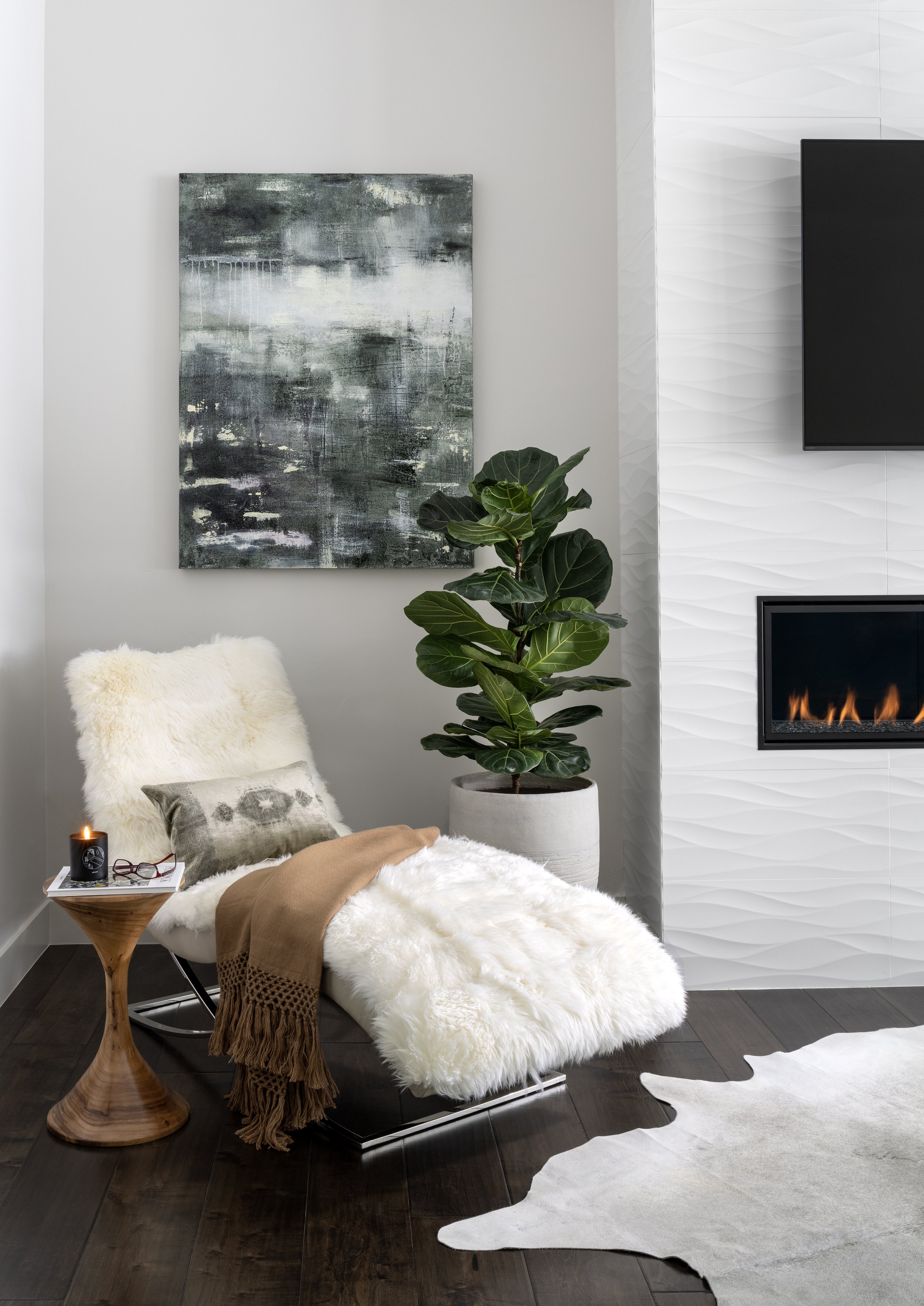 Textural lounge chair and side table beside a modern fireplace in a warm, neutral interior.