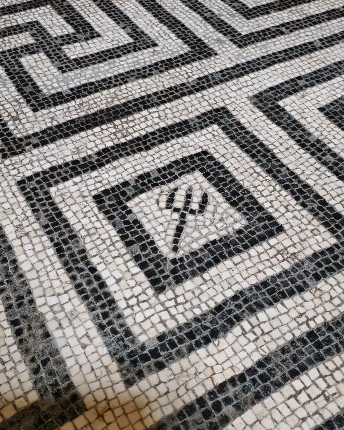Close-up of an ancient Roman mosaic floor, showing intricate pattern, texture, and craftsmanship shaped by time.