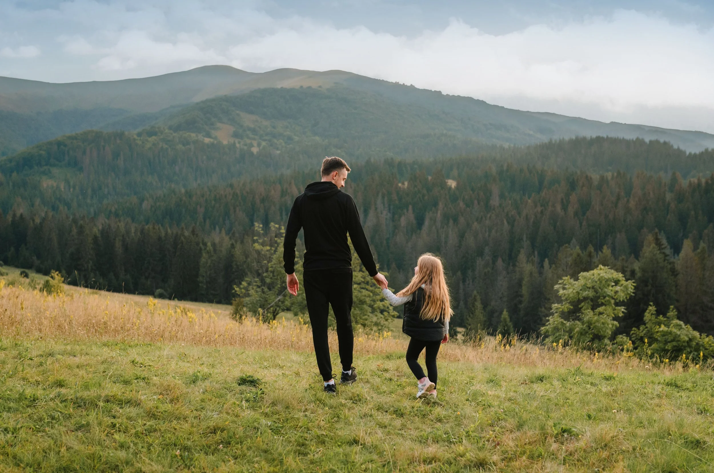 Father and daughter holding hands in front of a mountain