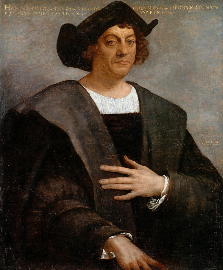A portrait of a man with short curly hair wearing a black hat, dark clothing, and a white shirt, with his right hand placed over his chest.