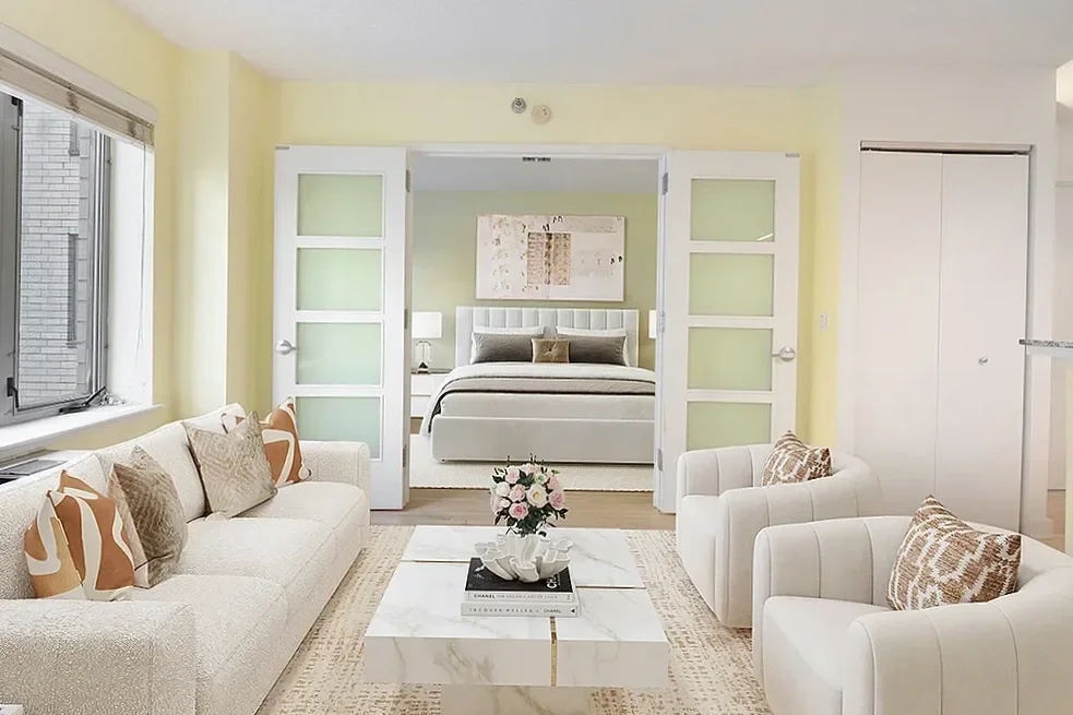 Bright living room with beige sofa, white armchairs, coffee tables, a large window showing a green yard, hardwood floors, decorative pillows, and wall art.