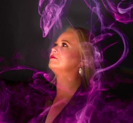 A woman with blonde hair looking upward, surrounded by swirling purple smoke or mist against a dark background.