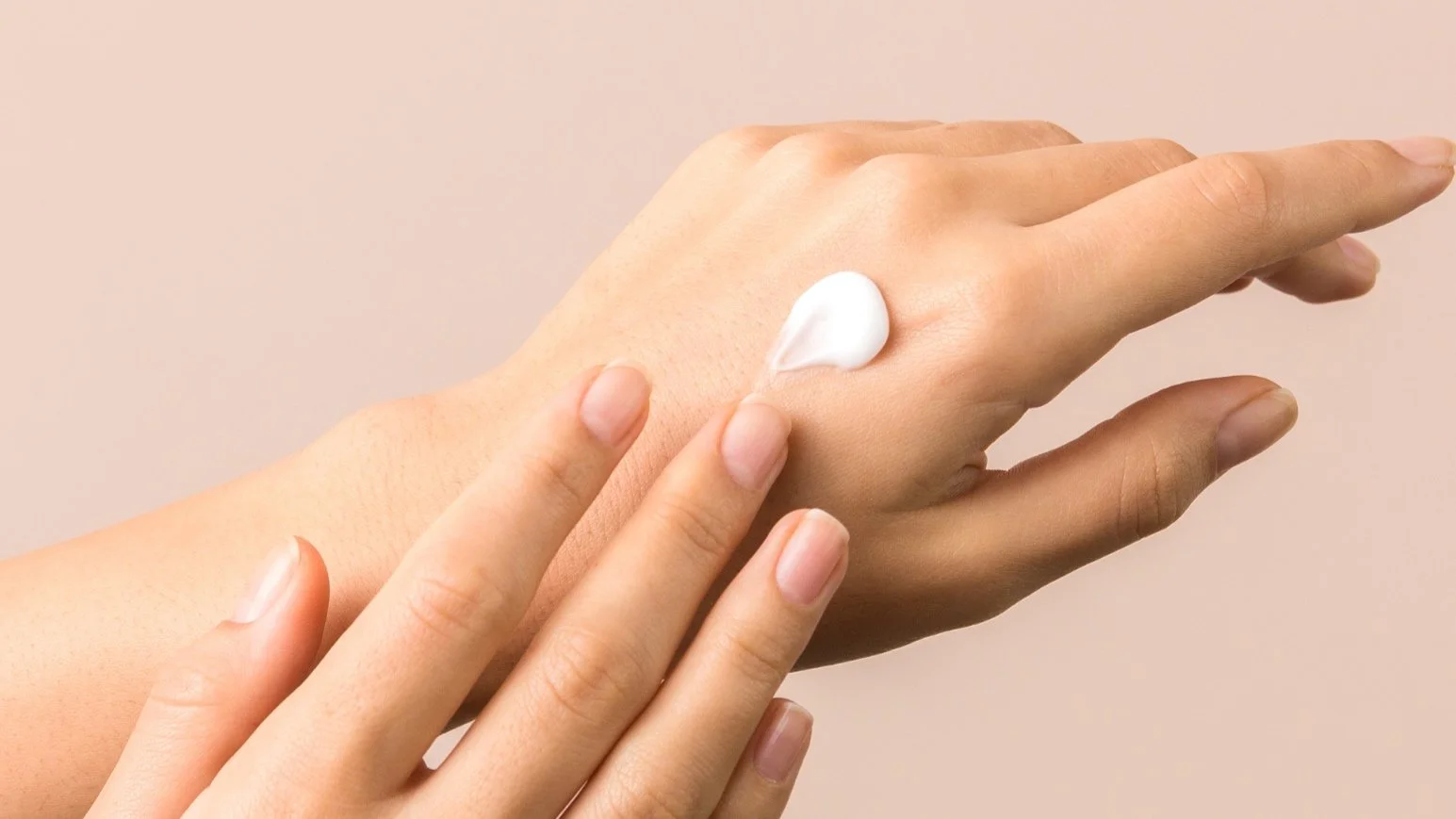 A person applying a dollop of white cream or lotion to the back of their hand.