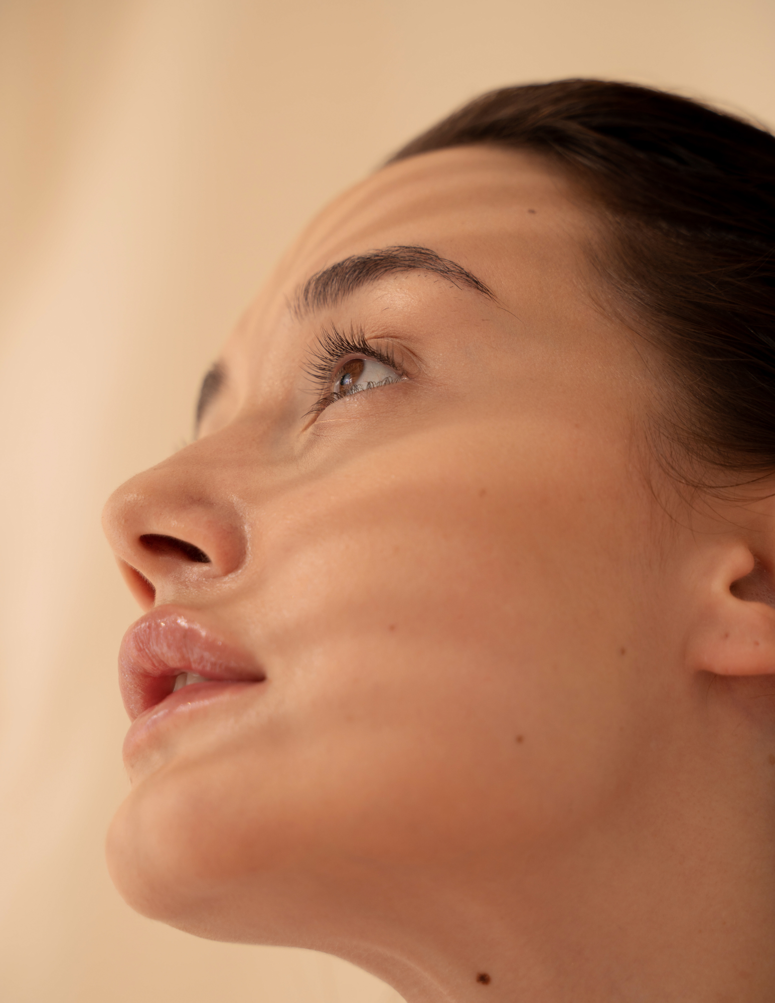 Close-up of a woman's face showing her side profile, focusing on her eye, nose, lips, and smooth skin.