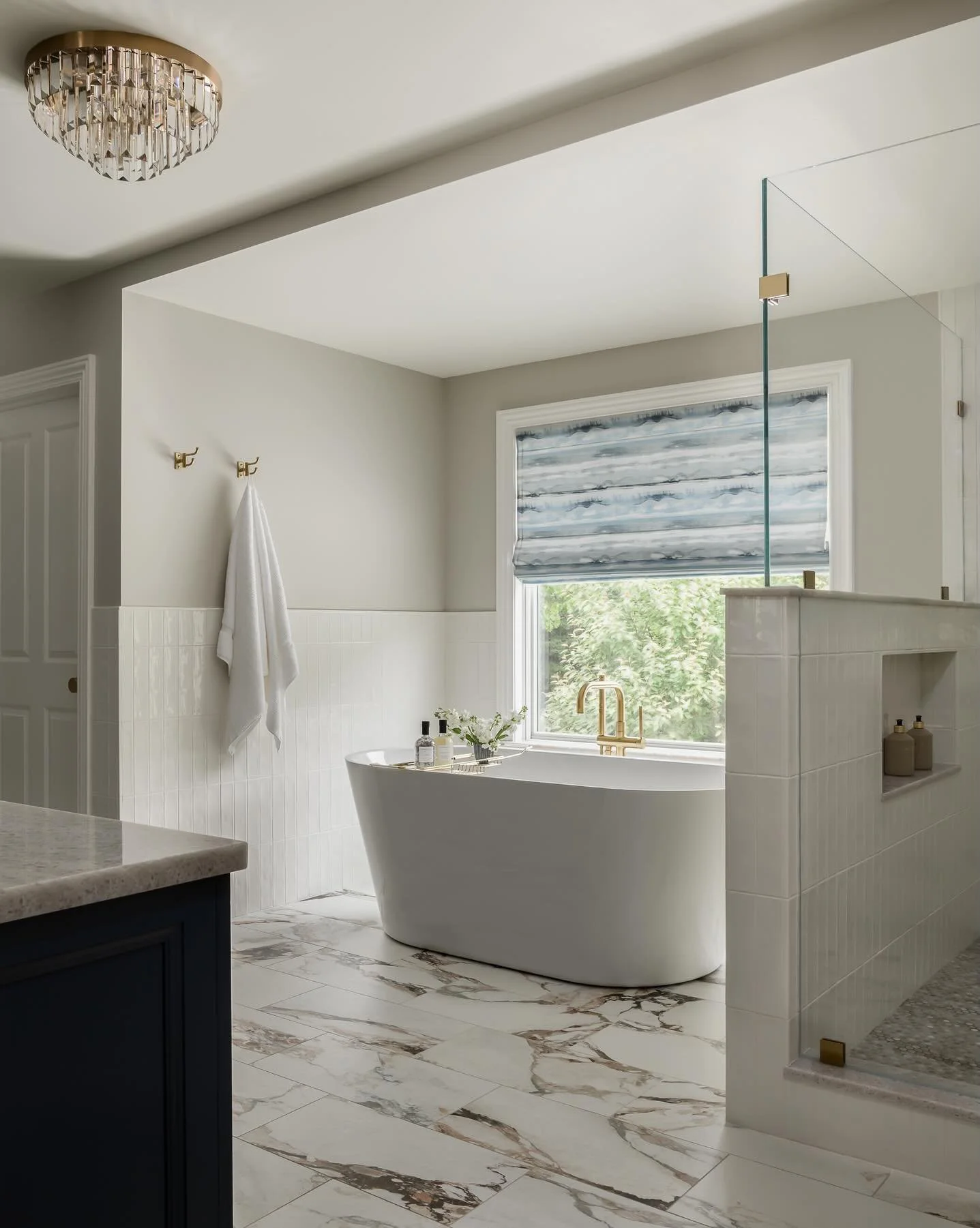 A primary bath built on quiet contrast.  Deep navy cabinetry, warm griege walls, brass layered throughout.
The floor does the talking.  Warm marble veining carried from the vanity through to the soaking tub and shower.  Watercolor stripe shades bring