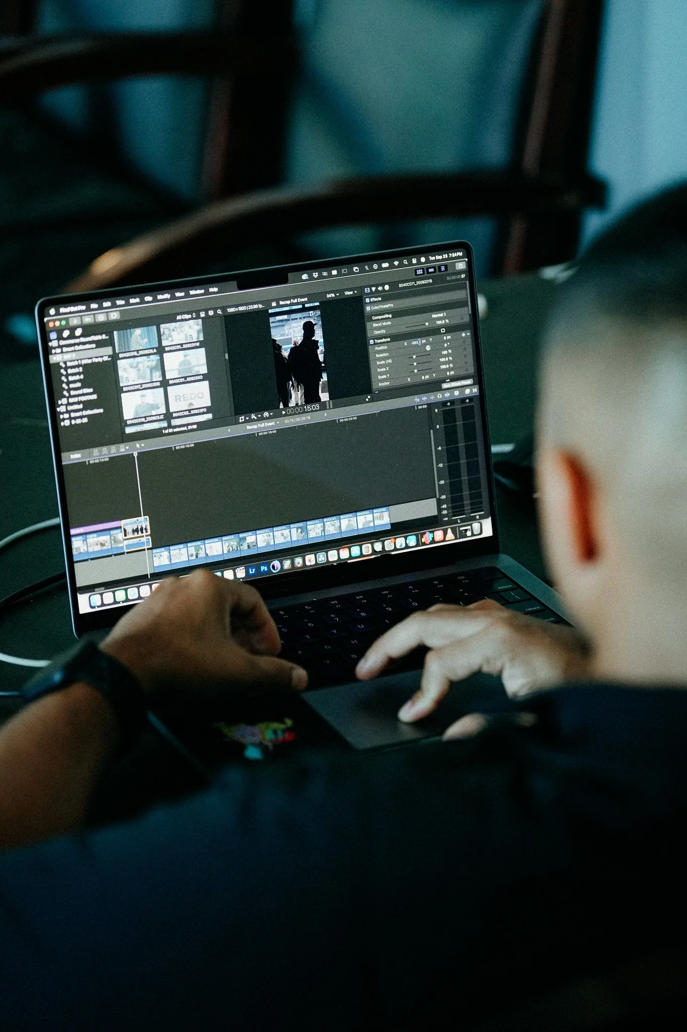 Person editing a video on a laptop with video editing software open, sitting on a dark surface with a chair in the background.