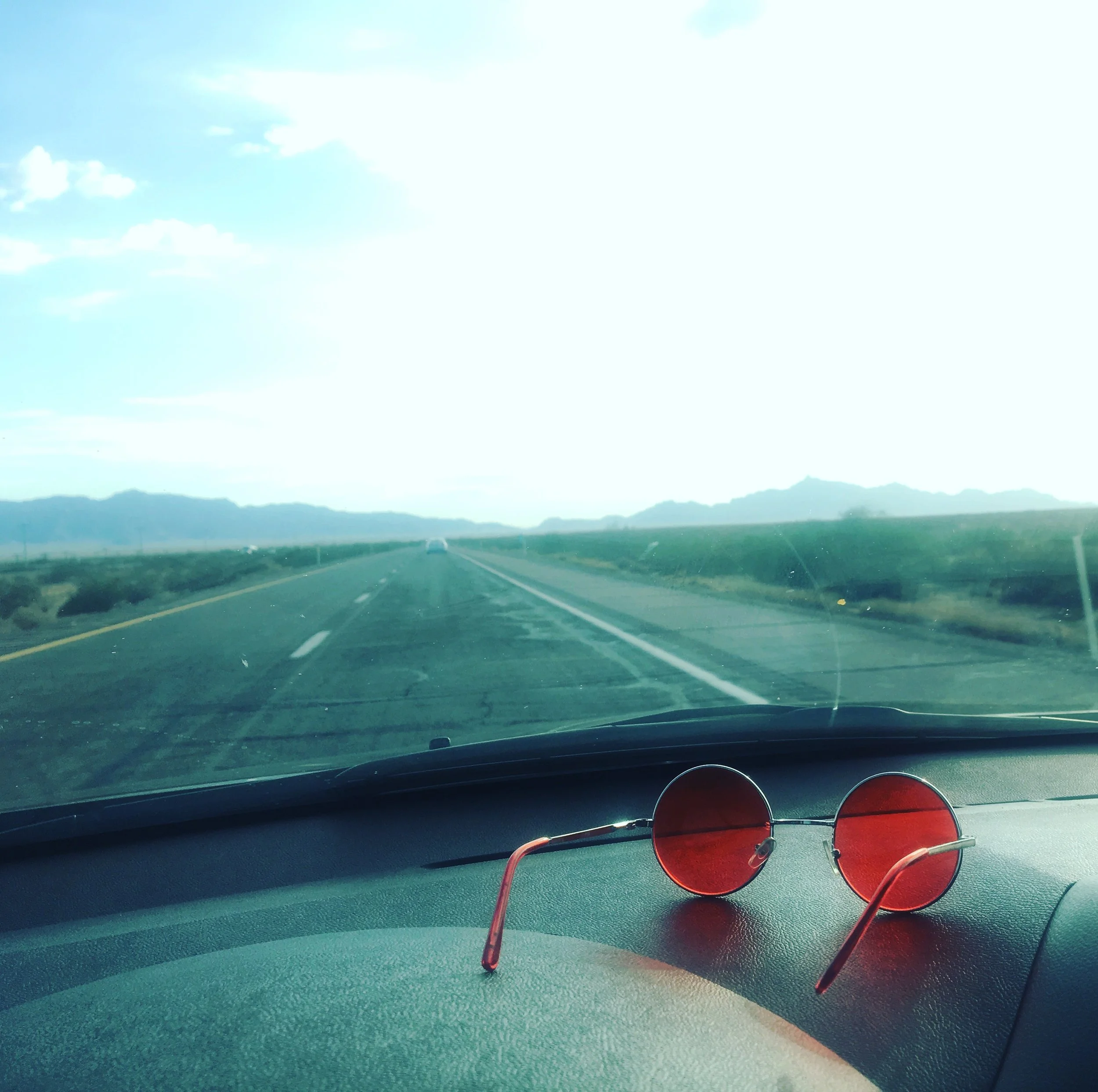 Red sunglasses resting on a dashboard during a Southwest desert road trip.