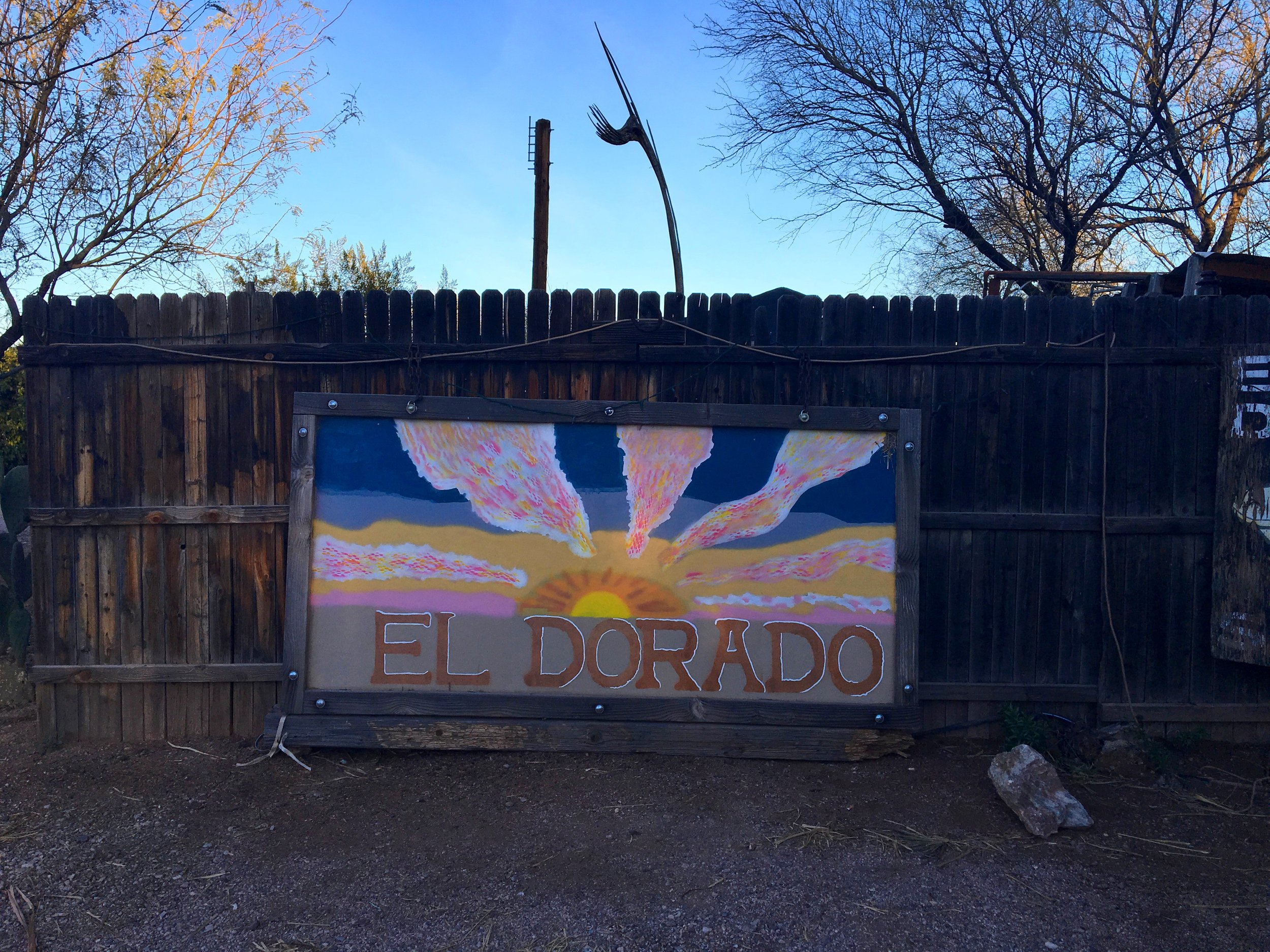 Entrance sign at El Dorado Hot Springs surrounded by desert fencing and palm trees in Tonopah, Arizona.