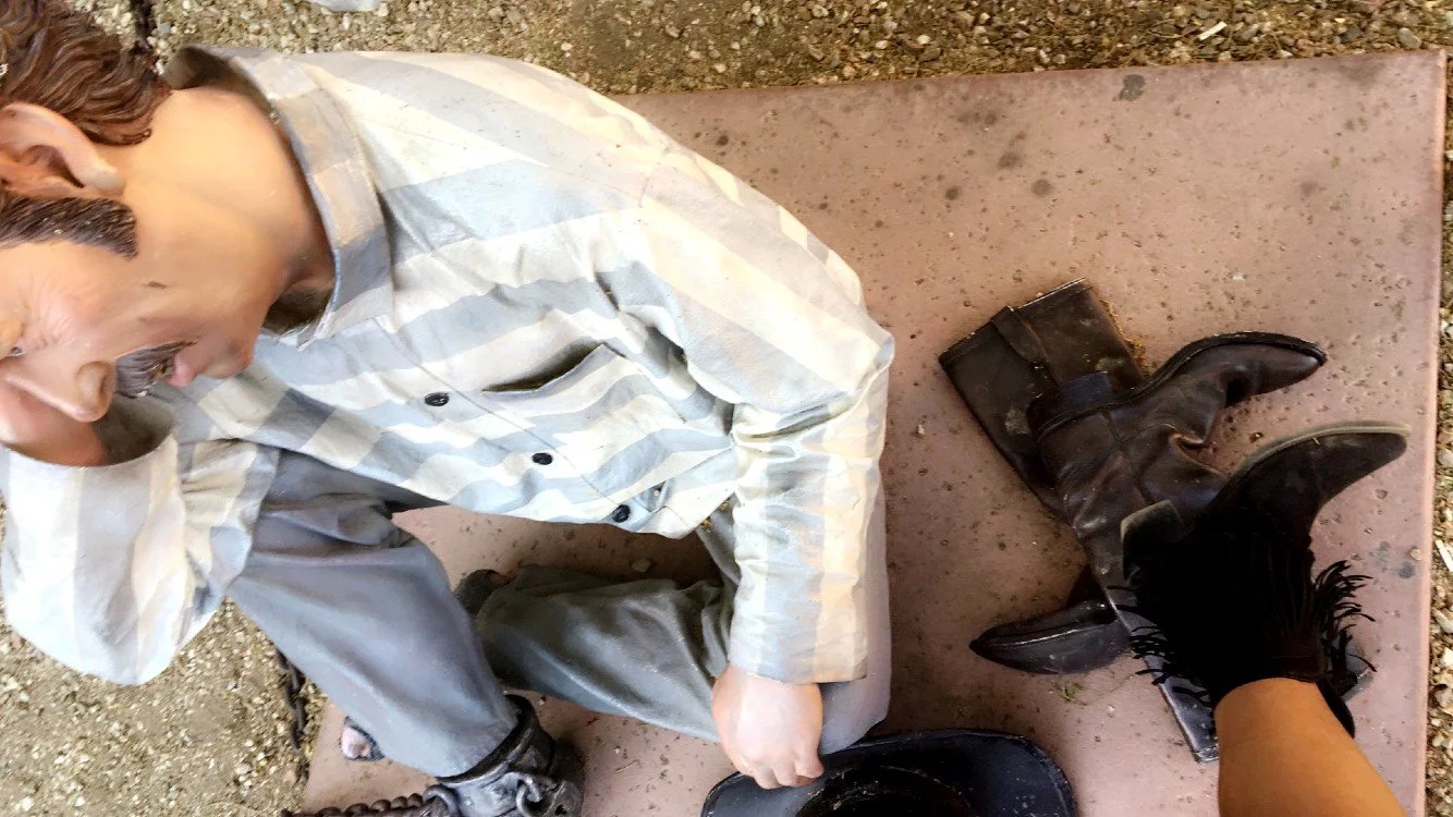 Overhead view of the prisoner statue at the Wickenburg Jail Tree with a pair of old boots and a visitor’s boot in the frame.