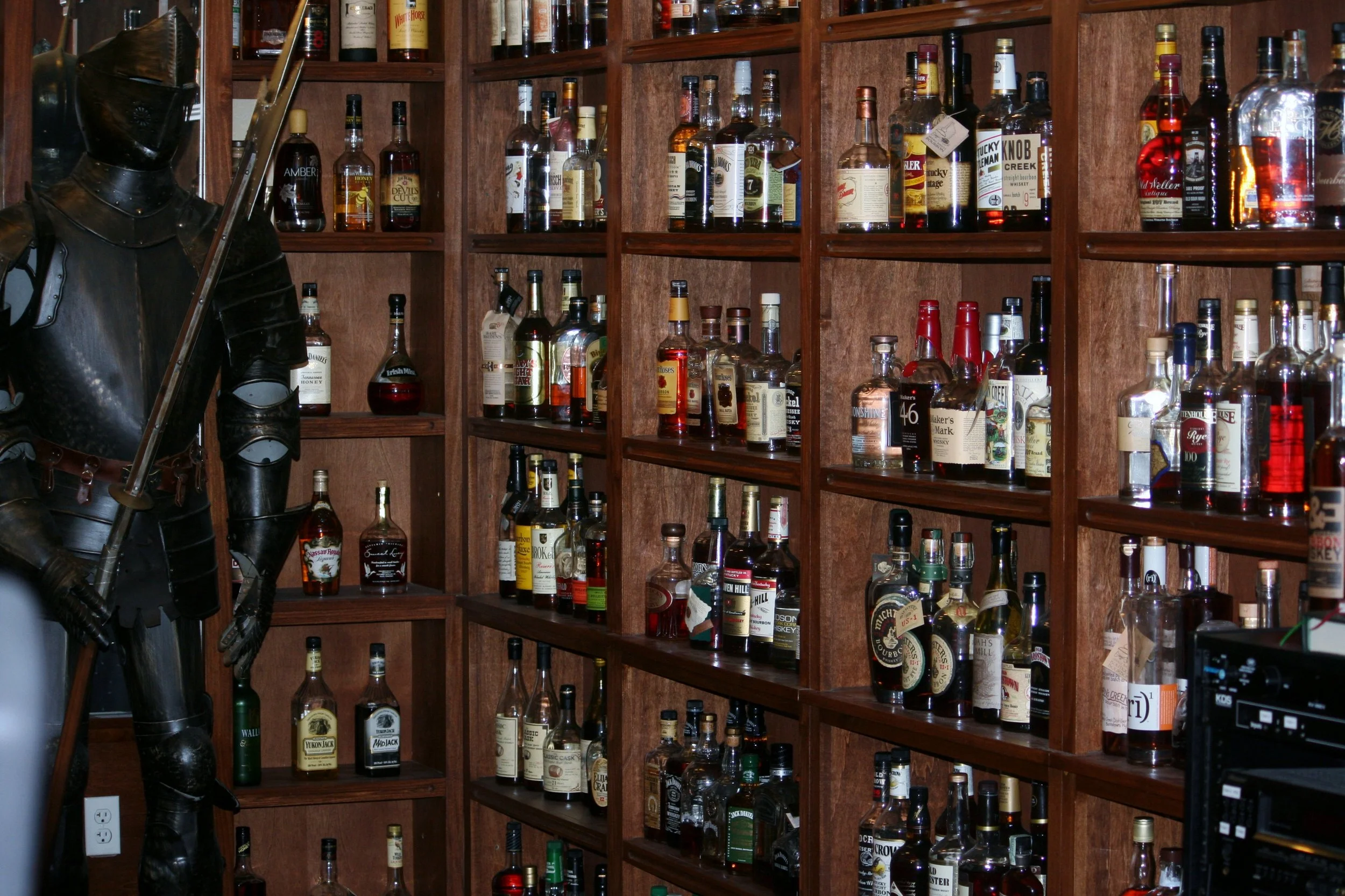 Large whiskey bottle collection displayed on wooden shelves beside a suit of armor inside a Las Vegas bar